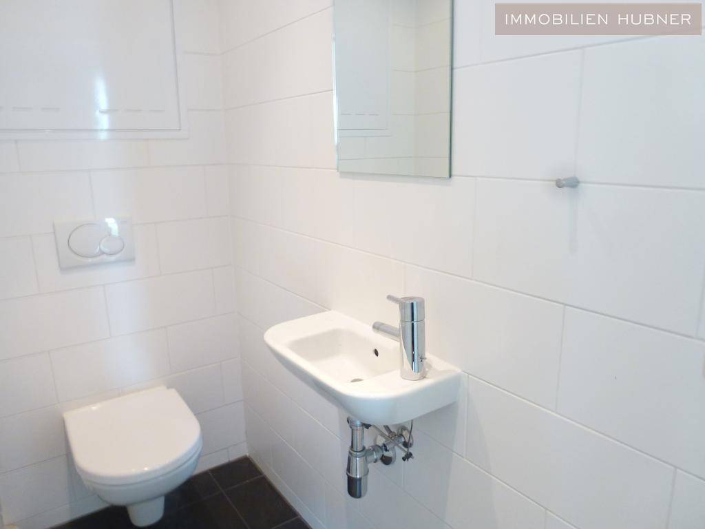 Helles Gäste-WC mit weißen Fliesen, wandhängendem WC und kleinem Waschbecken.