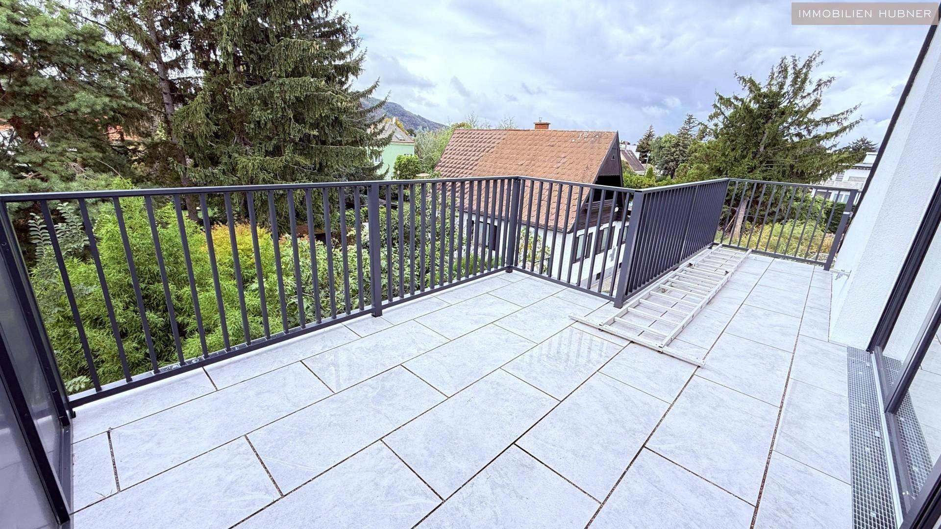 Geräumige Terrasse mit Fliesenboden und Metallgeländer, umgeben von viel Grün und Blick auf die Umgebung.