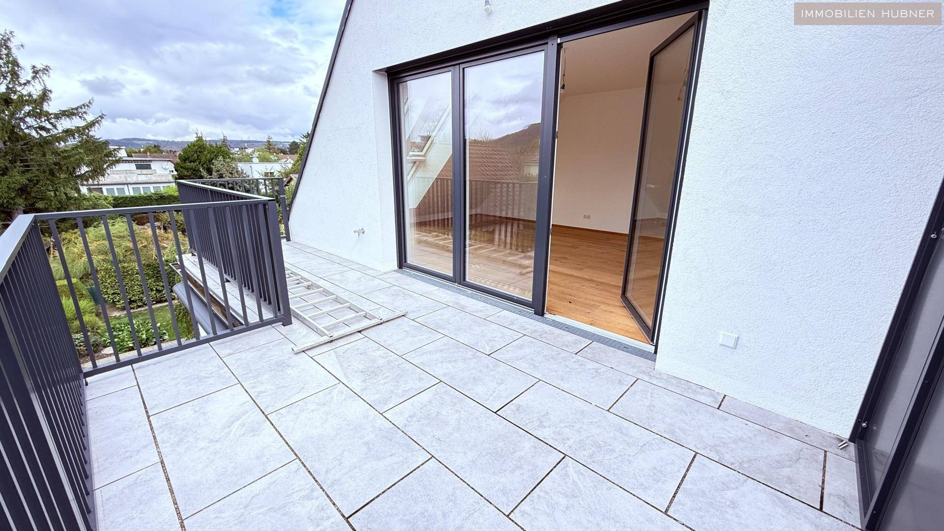Moderne Terrasse mit Fliesenboden und Zugang zu einem hellen Innenraum mit Holzboden.