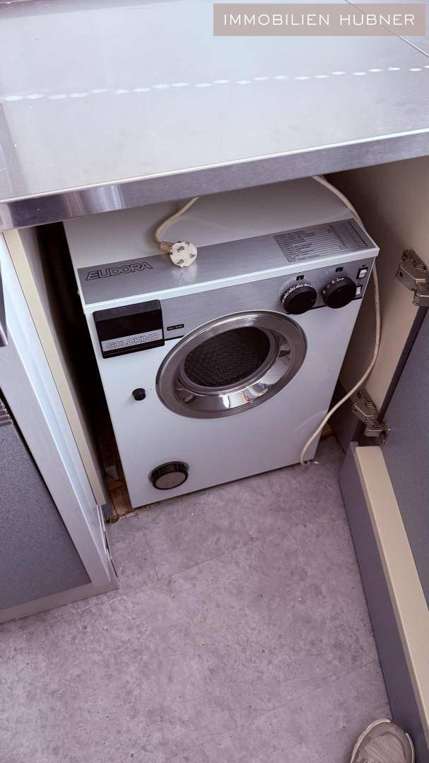 Eine Waschmaschine ist unter einer Arbeitsplatte in einem praktischen Hauswirtschaftsraum installiert.