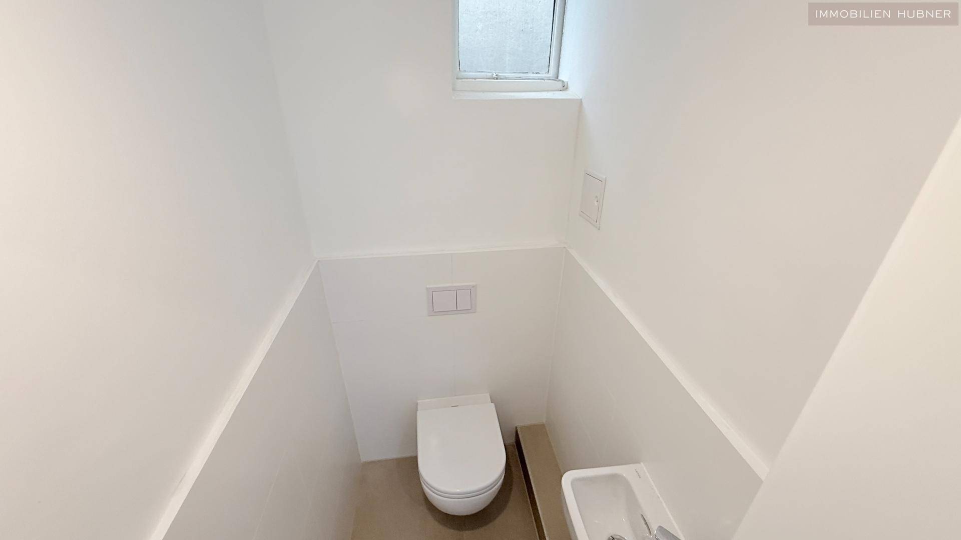 Kleines, helles Gäste-WC mit wandhängender Toilette und kleinem Handwaschbecken.