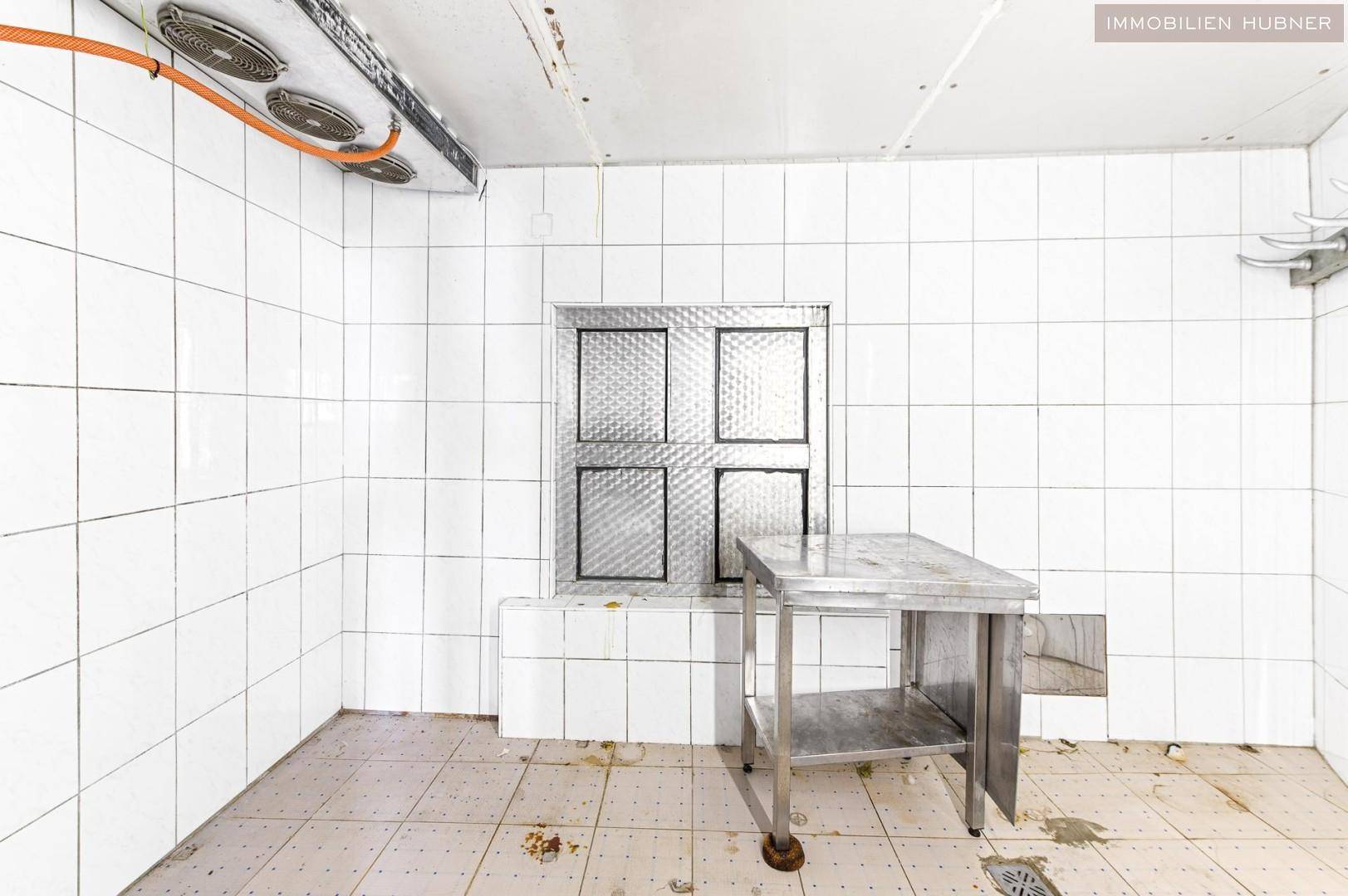 Sauberer Lagerraum mit weißen Fliesen, einem Edelstahltisch und Lüftungssystem an der Decke.