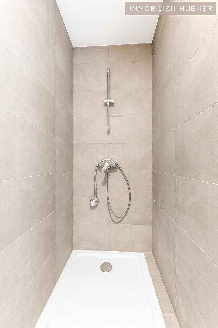 Modernes Badezimmer mit beigefarbenen Fliesen und einer begehbaren Dusche, minimalistisch gestaltet.