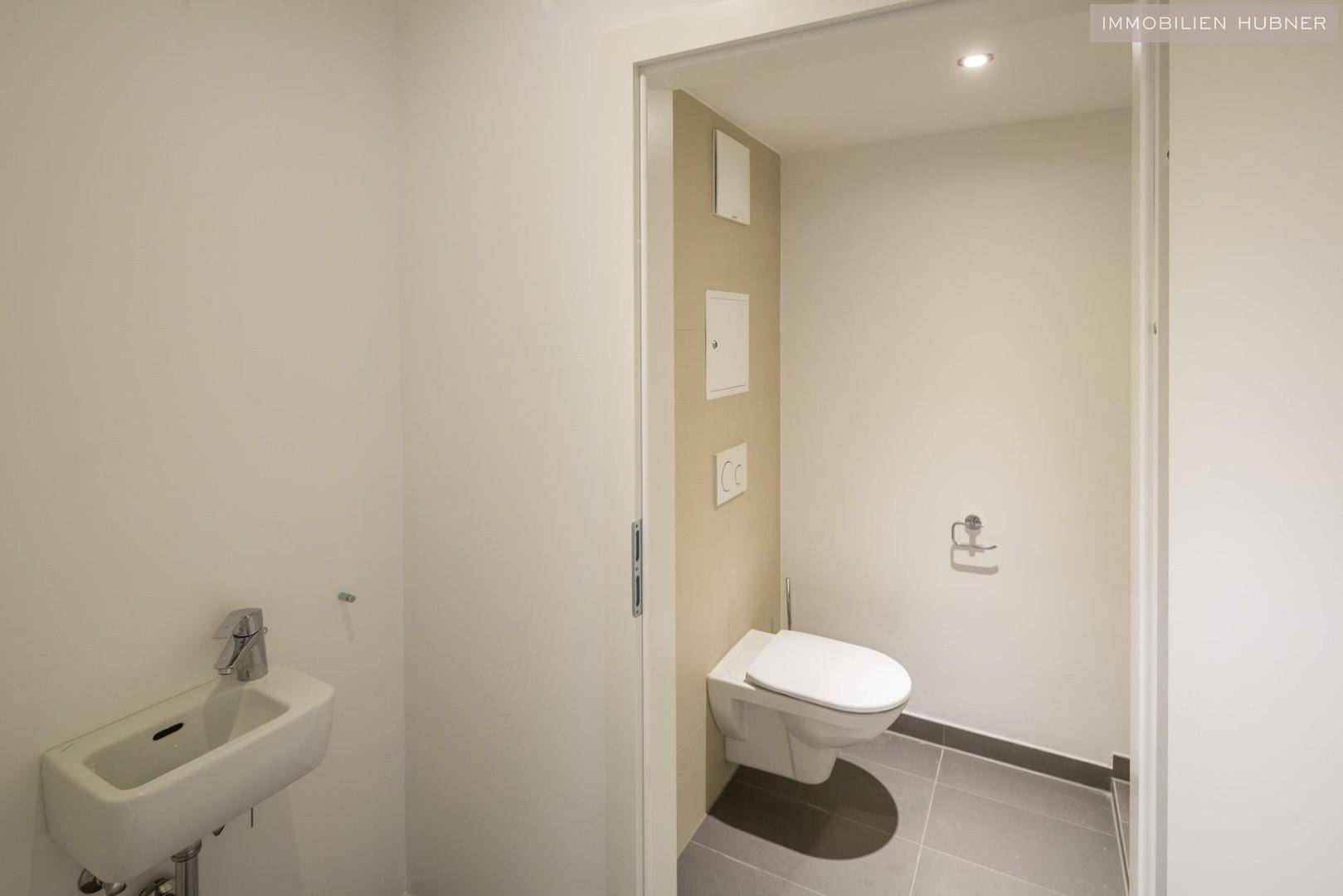 Modernes Gäste-WC mit wandhängender Toilette und kleinem Waschbecken, in neutralen Farben gehalten.
