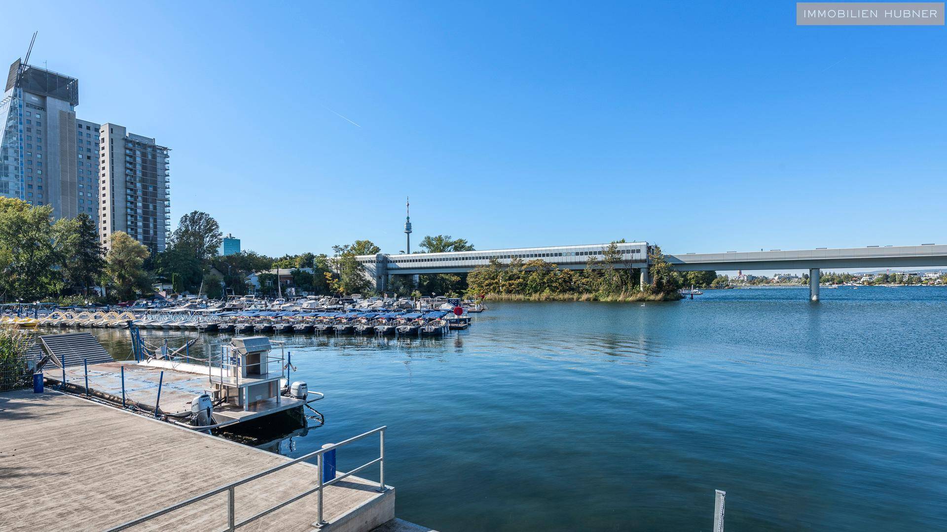 Weitläufiger Blick auf den See mit Bootsanlegestellen und einer Brücke im Hintergrund.
