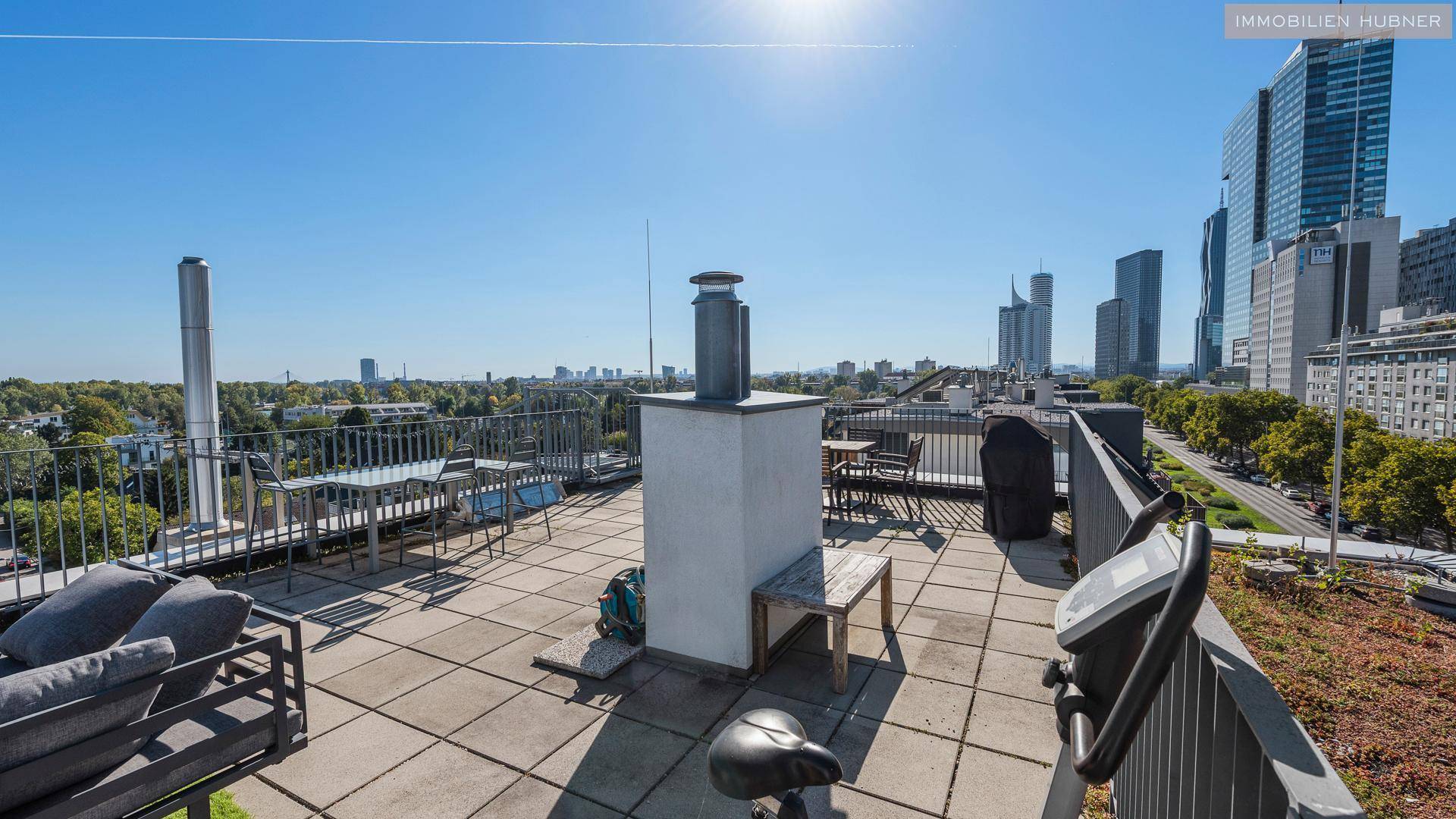 Geräumige Dachterrasse mit Stadtblick und Fitnessgerät unter blauem Himmel.