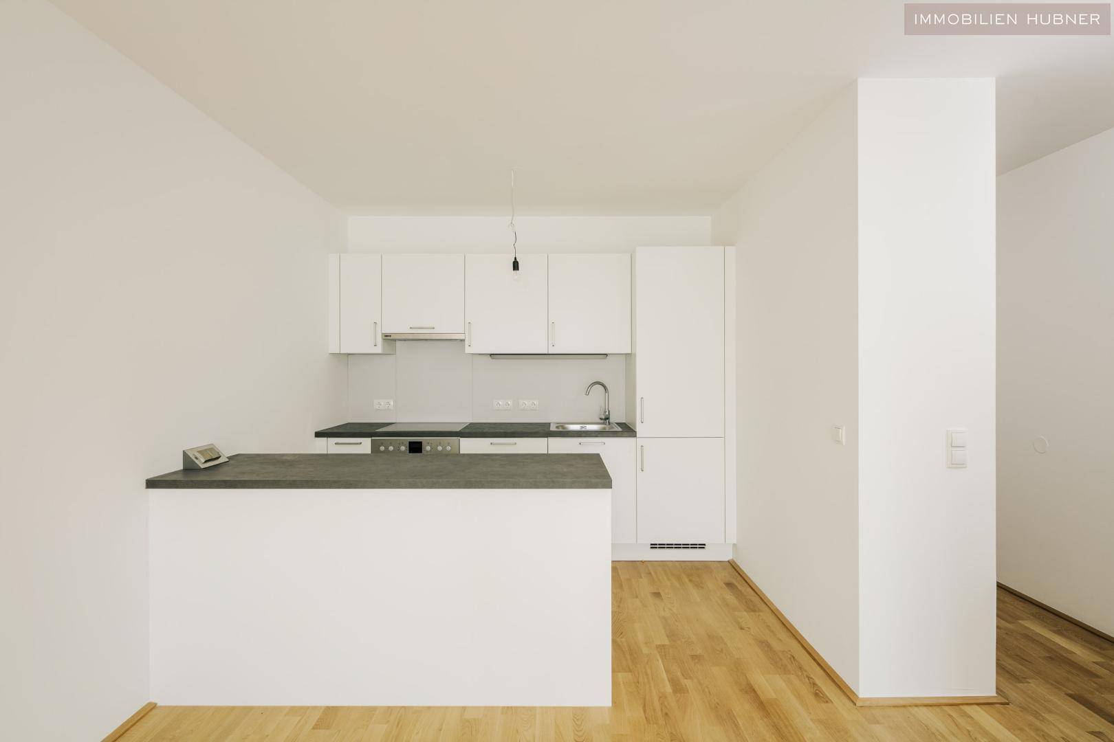 Moderne Einbauküche mit weißen Schränken, grauer Arbeitsplatte und Holzboden.