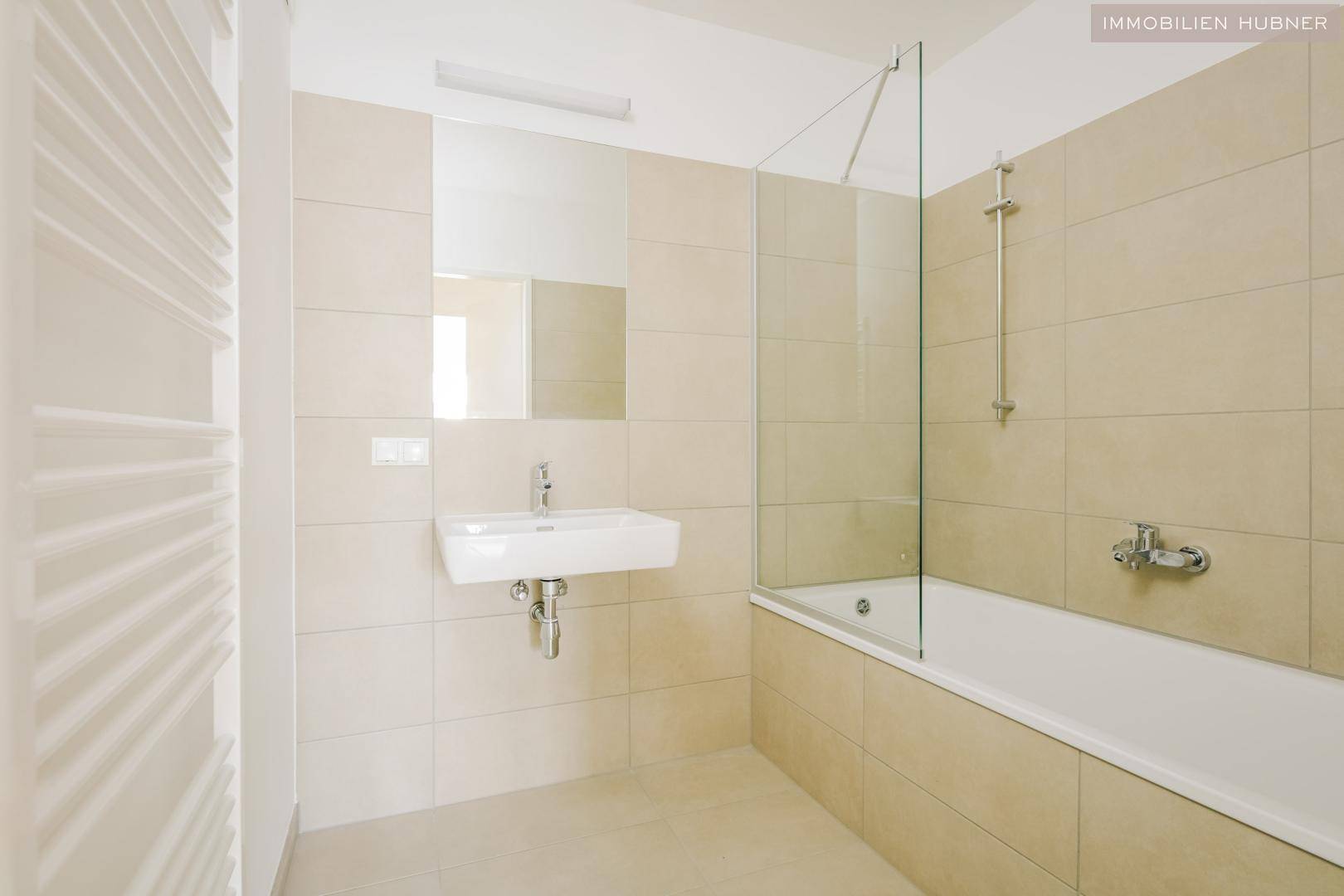 Modernes Badezimmer mit beigefarbenen Fliesen, Badewanne mit Duschwand und Handtuchheizkörper.