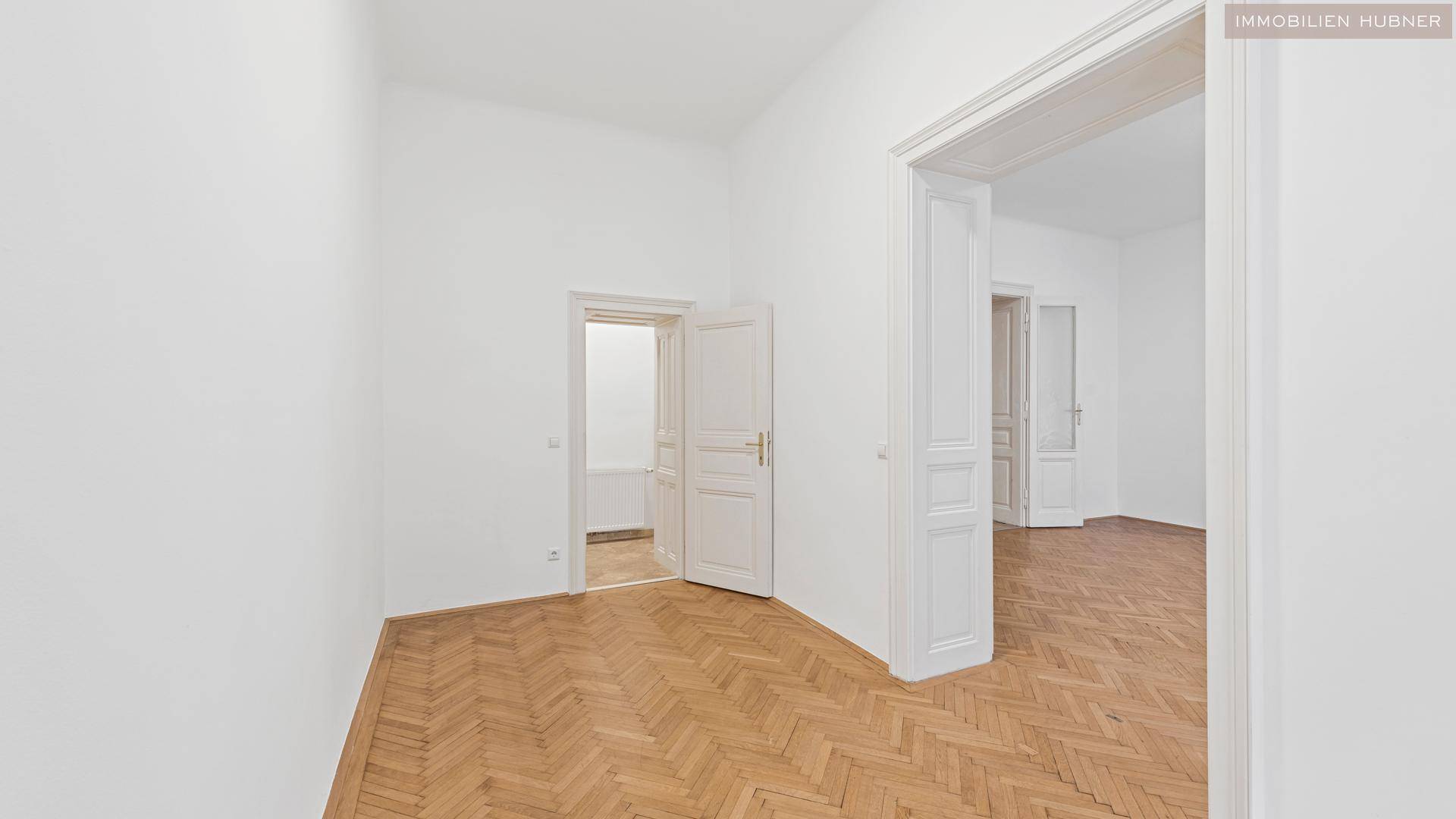 Helles Zimmer mit Fischgrätparkett und zwei offenen Durchgängen, die eine flexible Raumgestaltung ermöglichen.