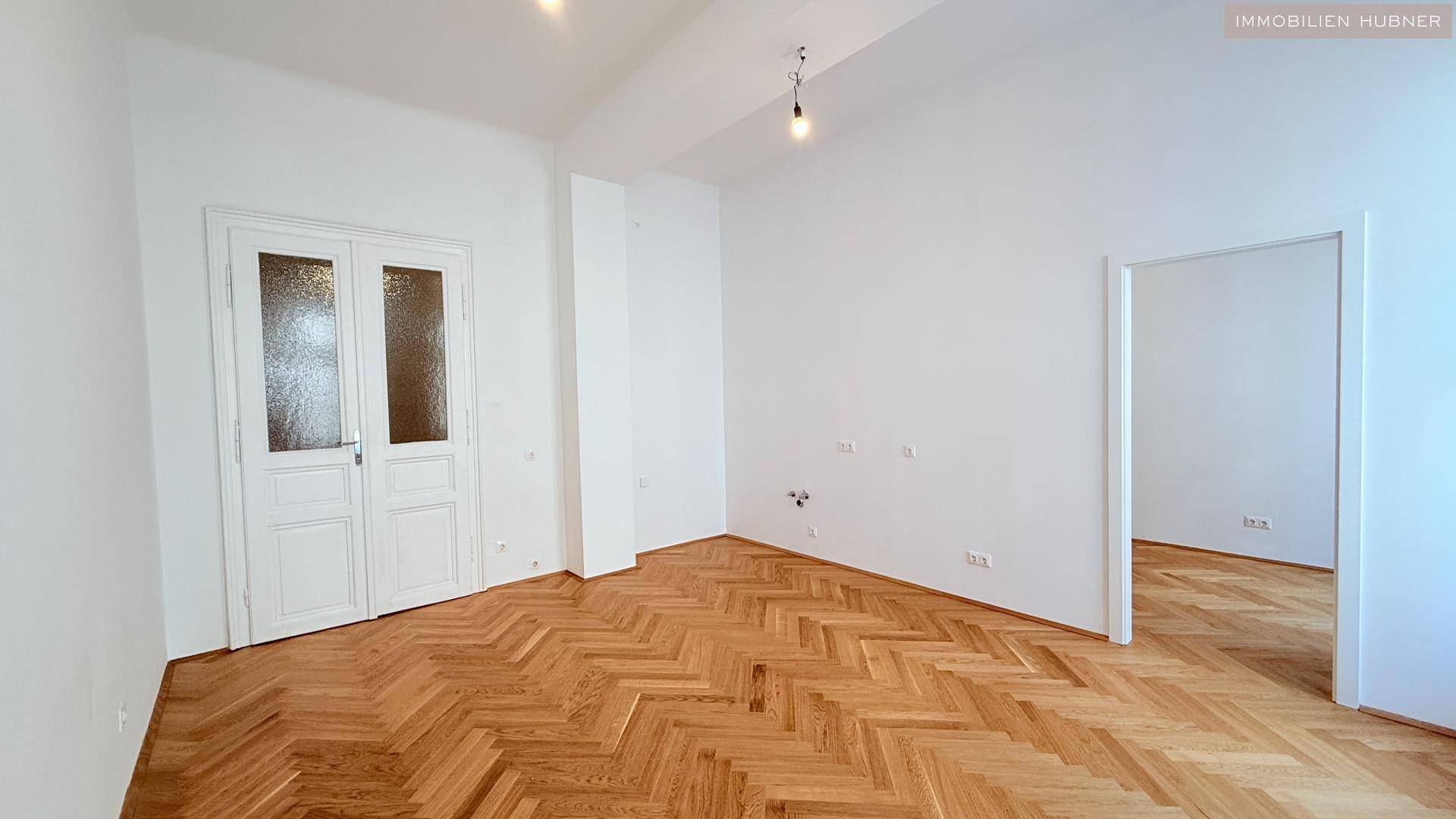 Geräumiges Zimmer mit klassischem Fischgrätparkett und hohen Decken, ideal für Wohnzwecke.