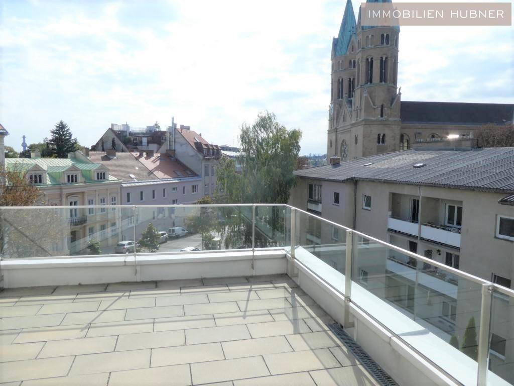 Geräumige Dachterrasse mit Fliesenboden und weitem Blick auf die Stadt und eine Kirche.