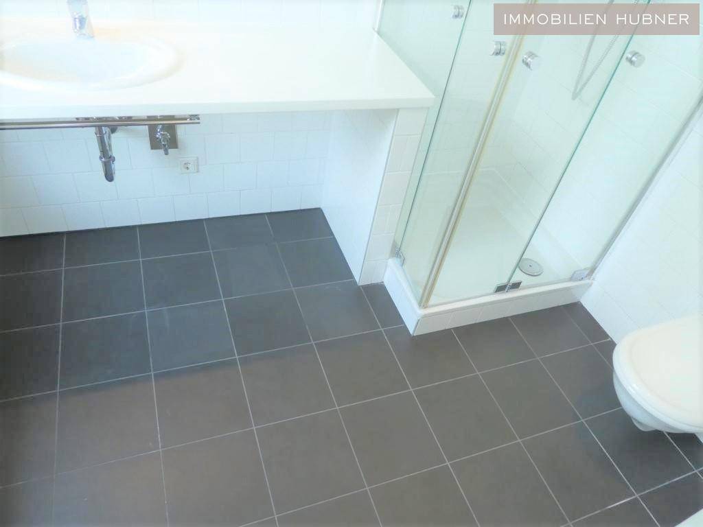 Modernes Badezimmer mit Duschkabine, Waschbecken und dunklem Fliesenboden.