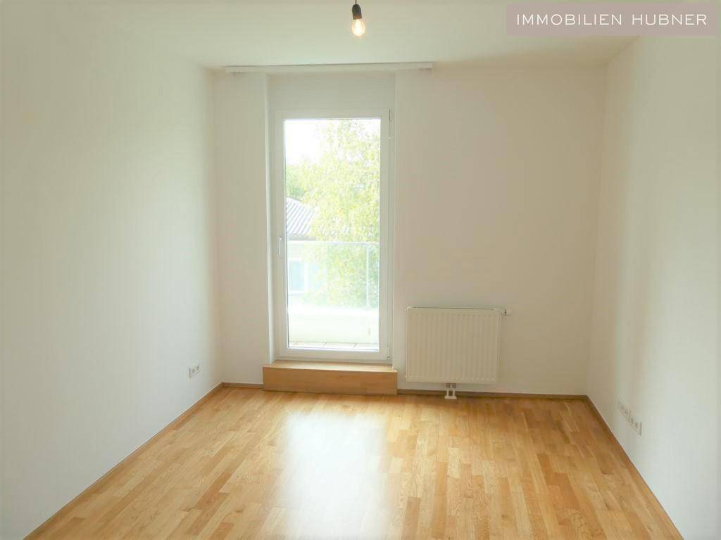 Helles Schlafzimmer mit Parkettboden und Zugang zu einem französischen Balkon.