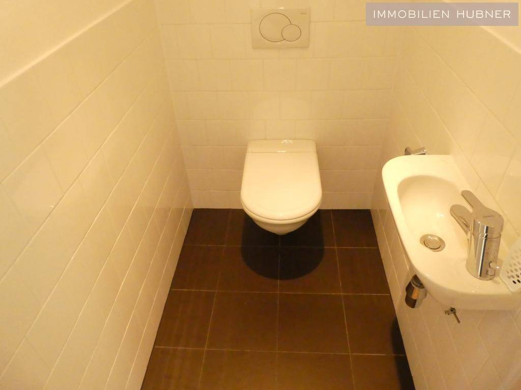 Kleines Gäste-WC mit Wand-WC, Waschbecken und Fliesenboden in Braun und Weiß.