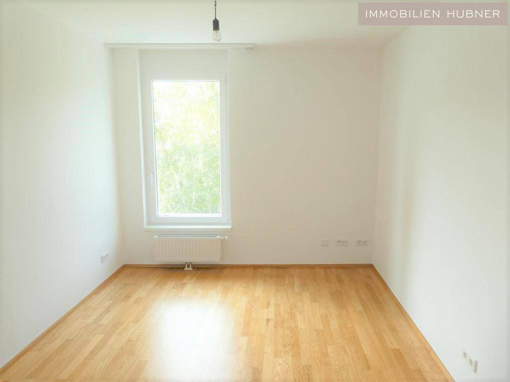 Einfaches Schlafzimmer mit Parkettboden und einem Fenster, das viel Licht spendet.
