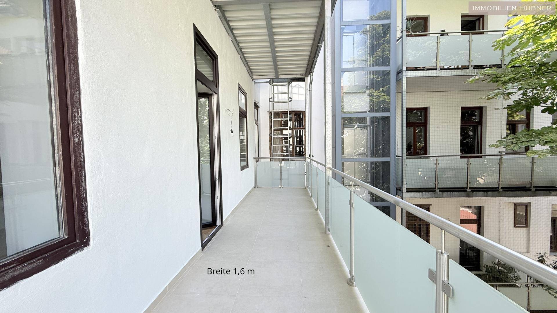 Langer, schmaler Balkon mit modernem Glasgeländer und Blick auf die umliegenden Gebäude.