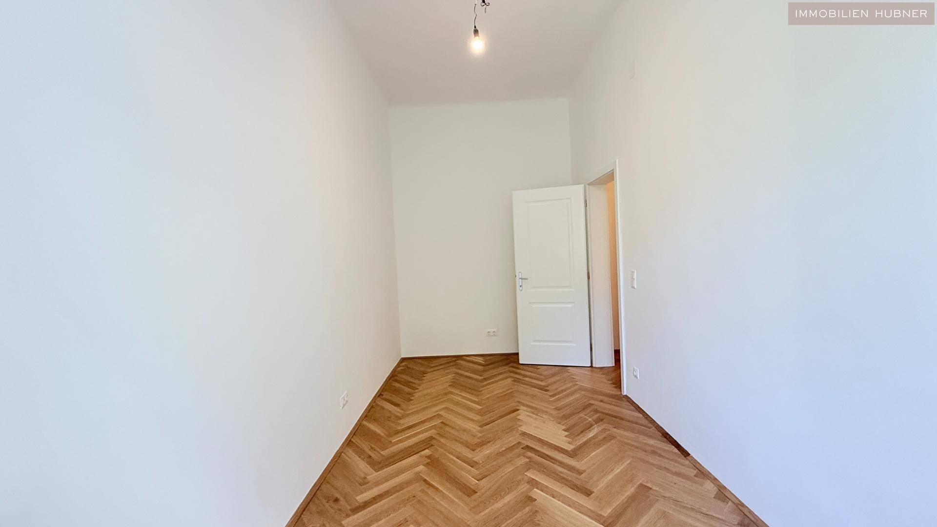 Schlichter Raum mit Fischgrätparkett und weiß gestrichenen Wänden, ideal als Schlafzimmer.