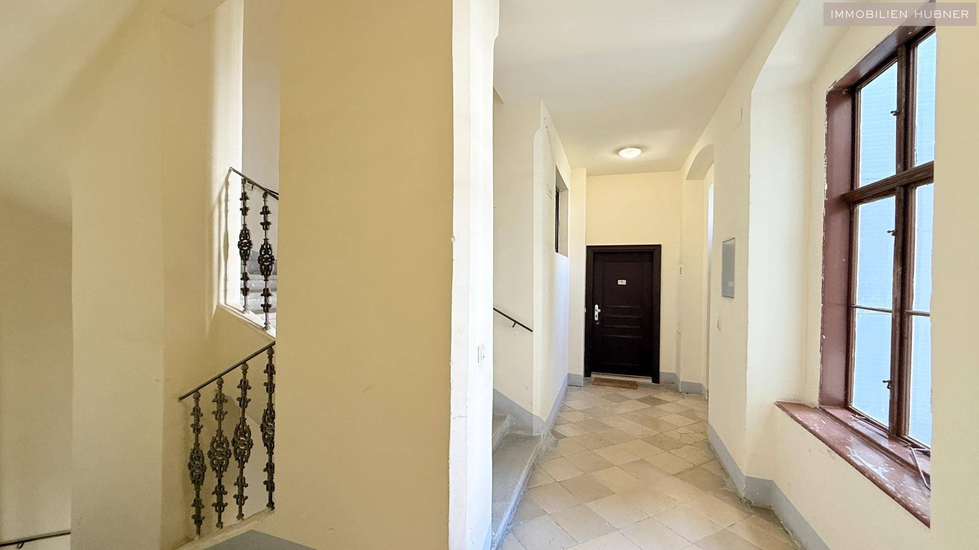 Heller Hausflur mit Fliesenboden und einer eleganten Treppe mit schmiedeeisernem Geländer.
