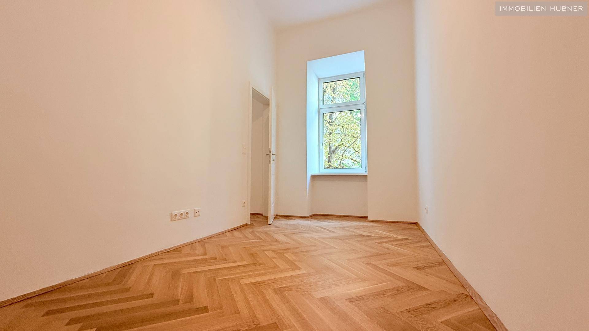 Helles Zimmer mit Fischgrätparkettboden und einem Fenster, ideal als Schlaf- oder Arbeitszimmer.