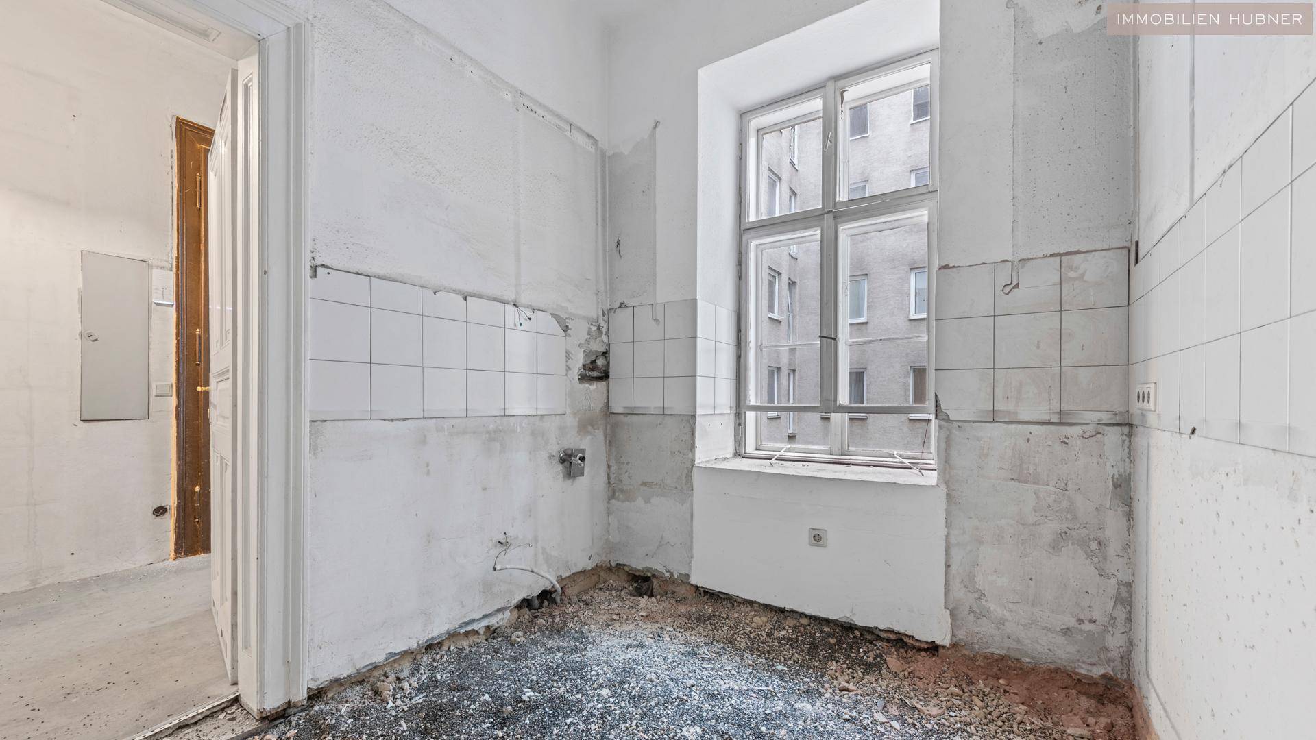Renovierungsbedürftige Küche mit gefliesten Wänden und einem Fenster mit Blick auf die Umgebung.
