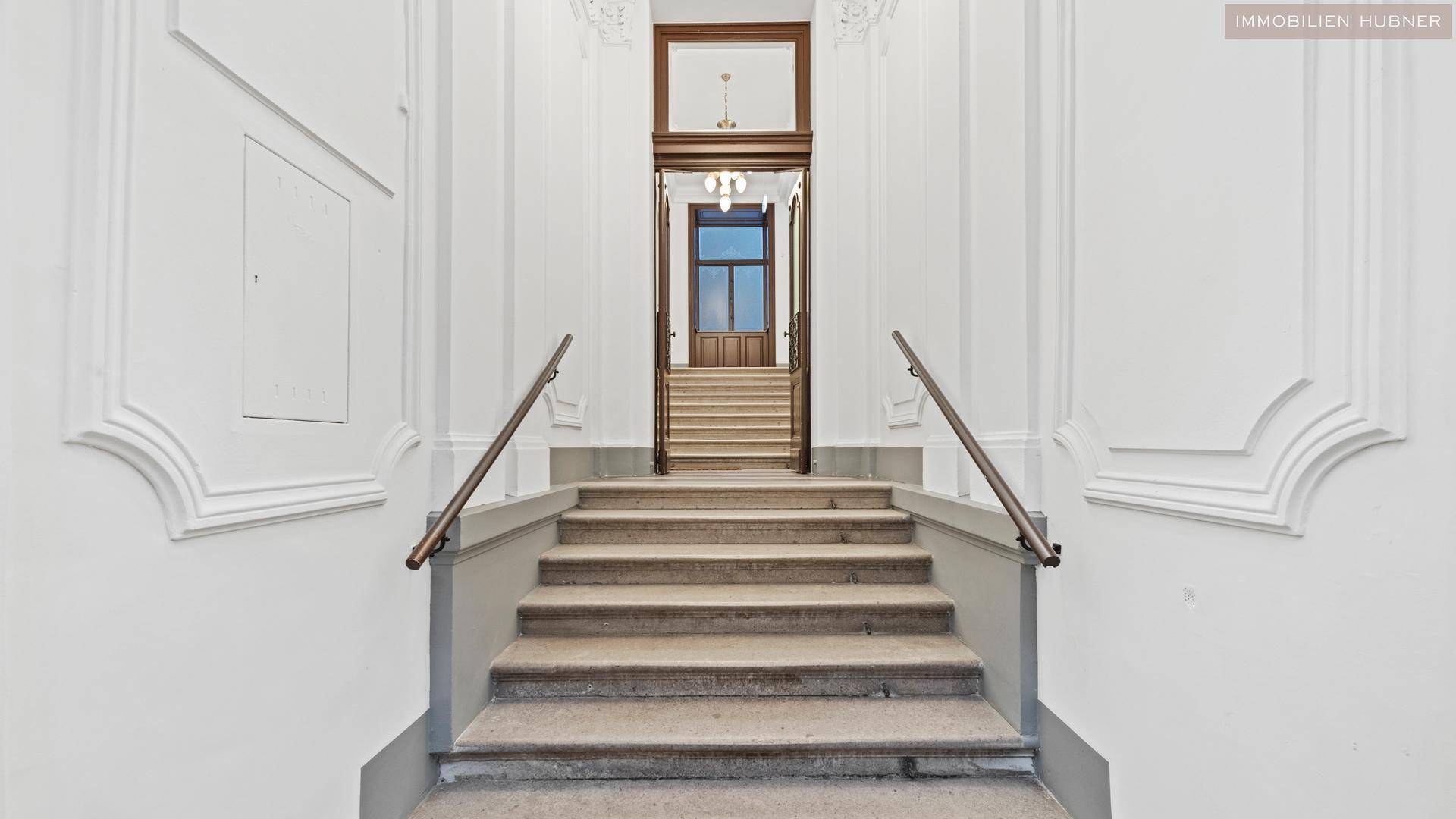 Repräsentativer Eingangsbereich mit breiter Treppe und eleganten architektonischen Details im Altbau.
