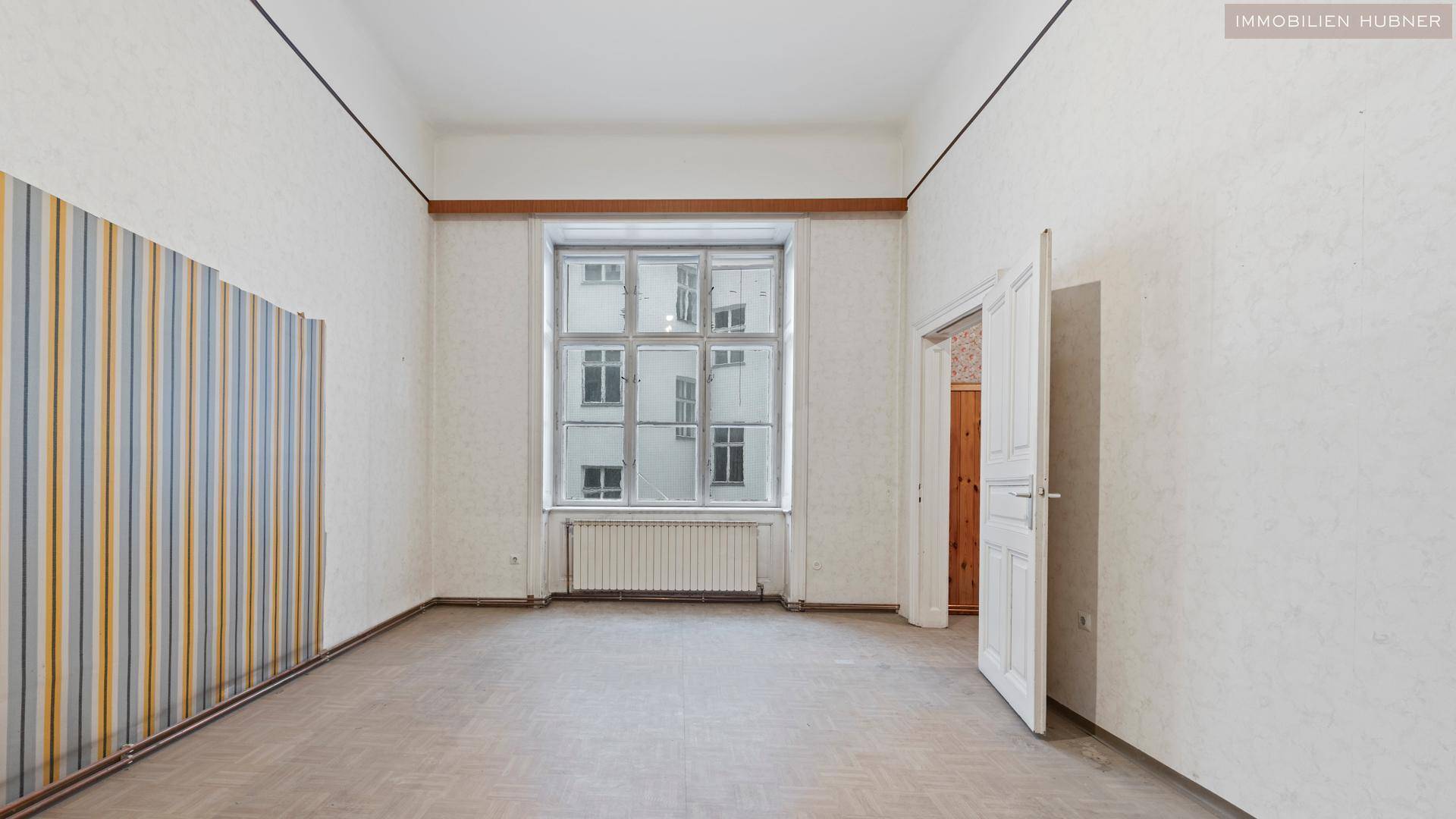 Heller, leerer Raum mit großem Fenster und gestreifter Tapete, bereit zur Neugestaltung.