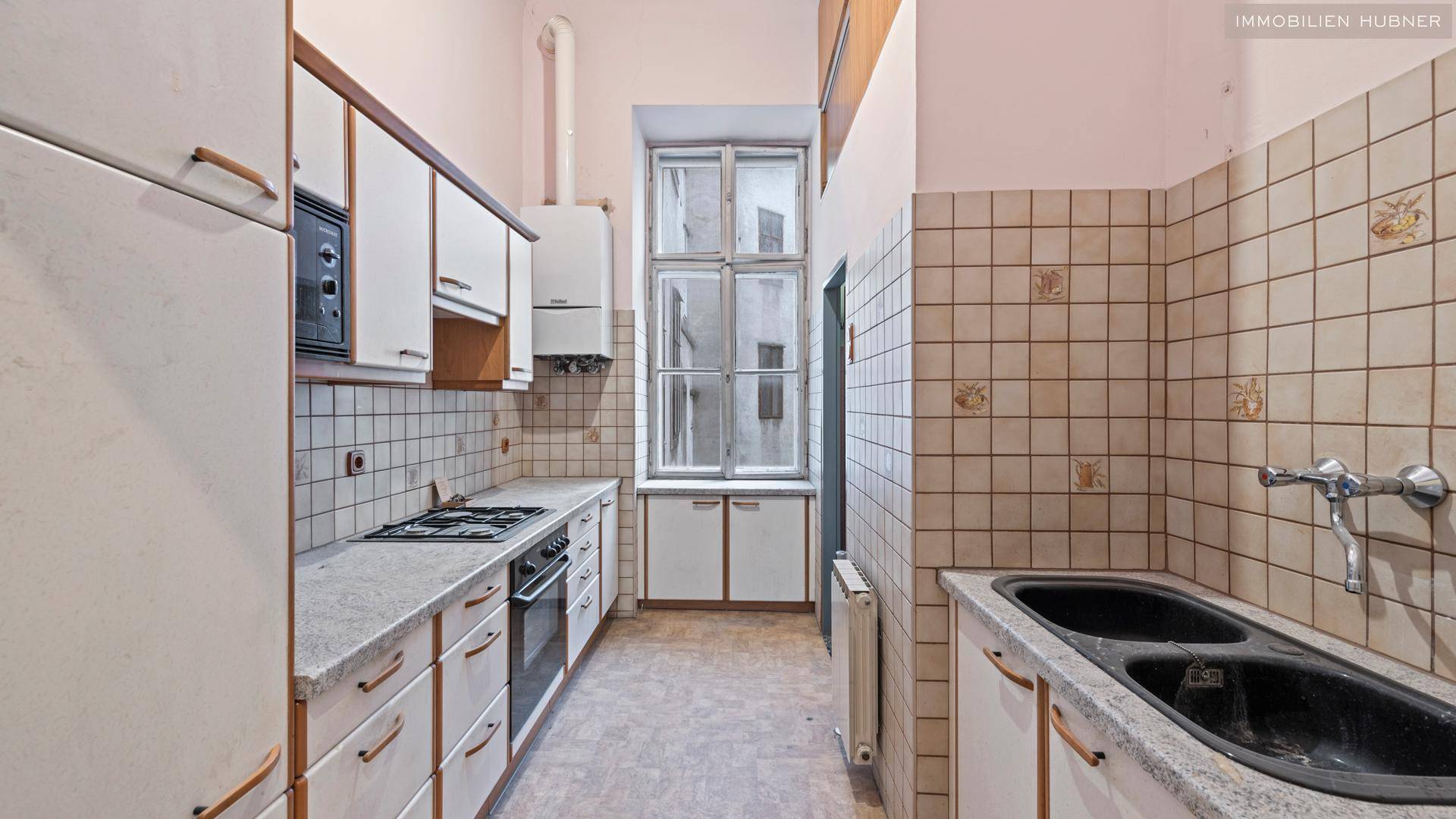 Renovierungsbedürftige Küche mit älteren Einbauschränken, Gasherd und Doppelspüle.