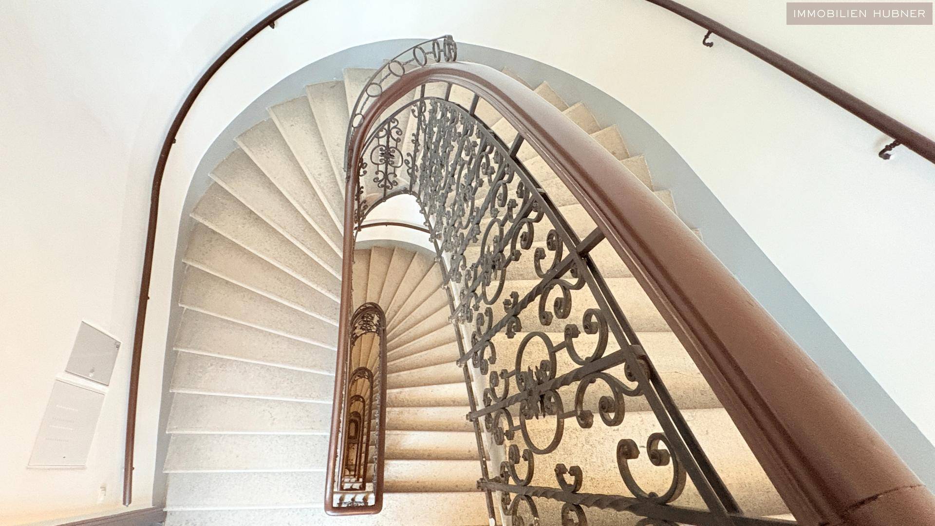 Elegantes Treppenhaus mit geschwungenen Stufen und kunstvollem Geländer in einem Altbau.
