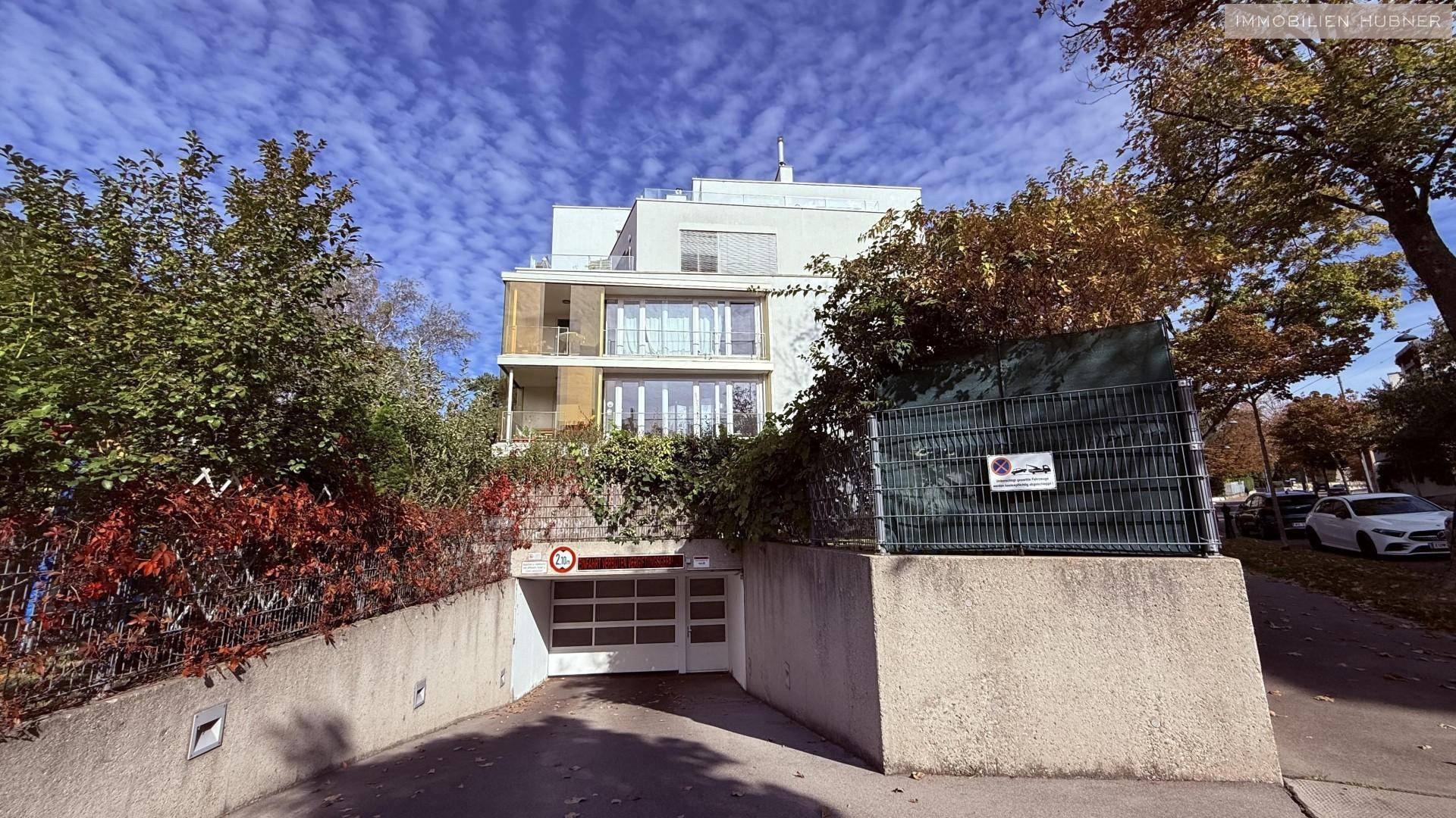 Moderne Wohnanlage mit Tiefgaragenzufahrt, umgeben von Bäumen und Sträuchern.