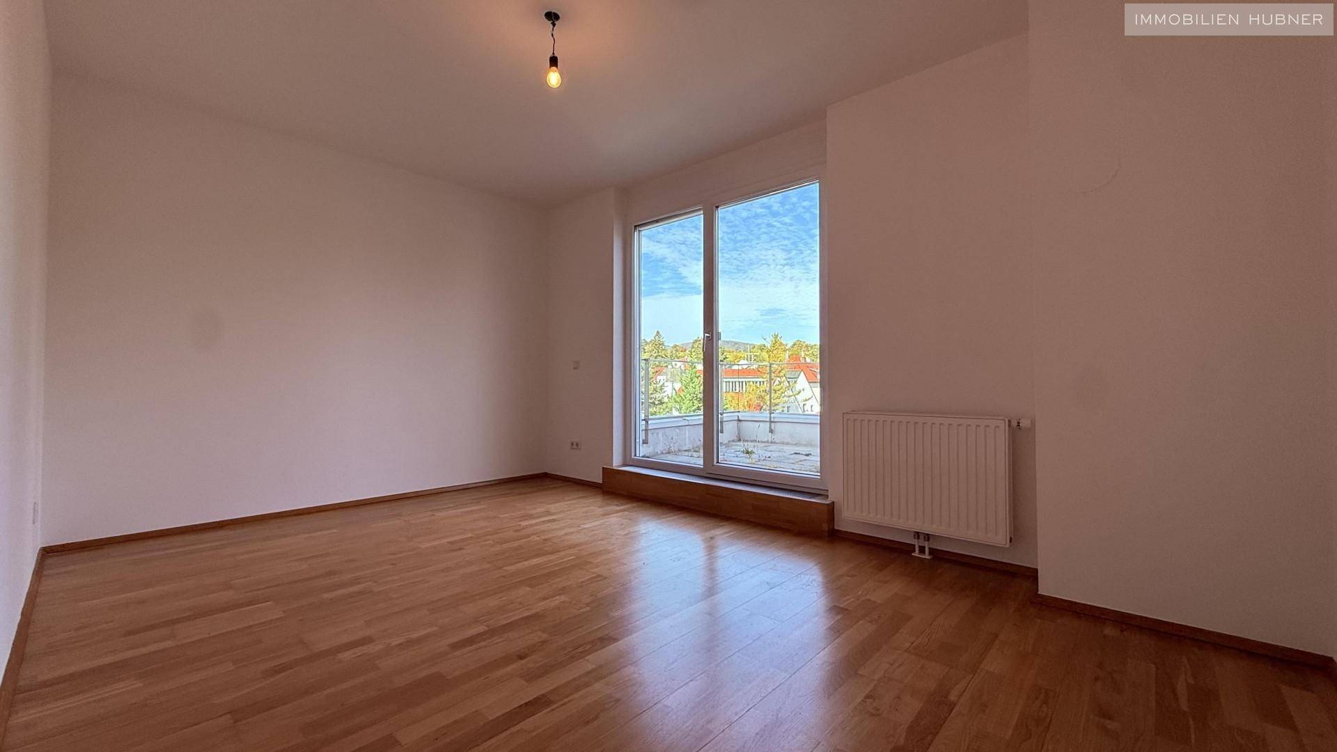 Geräumiges Zimmer mit Parkettboden und großen Fenstern, die viel Tageslicht hereinlassen.