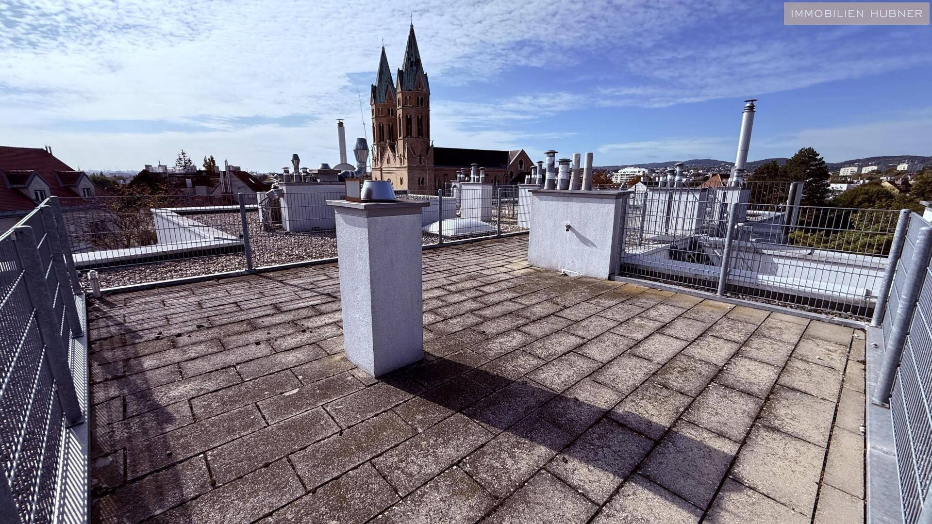 Weitläufige Dachterrasse mit Fliesenboden und Metallgeländer, bietet einen Panoramablick über die Stadt.