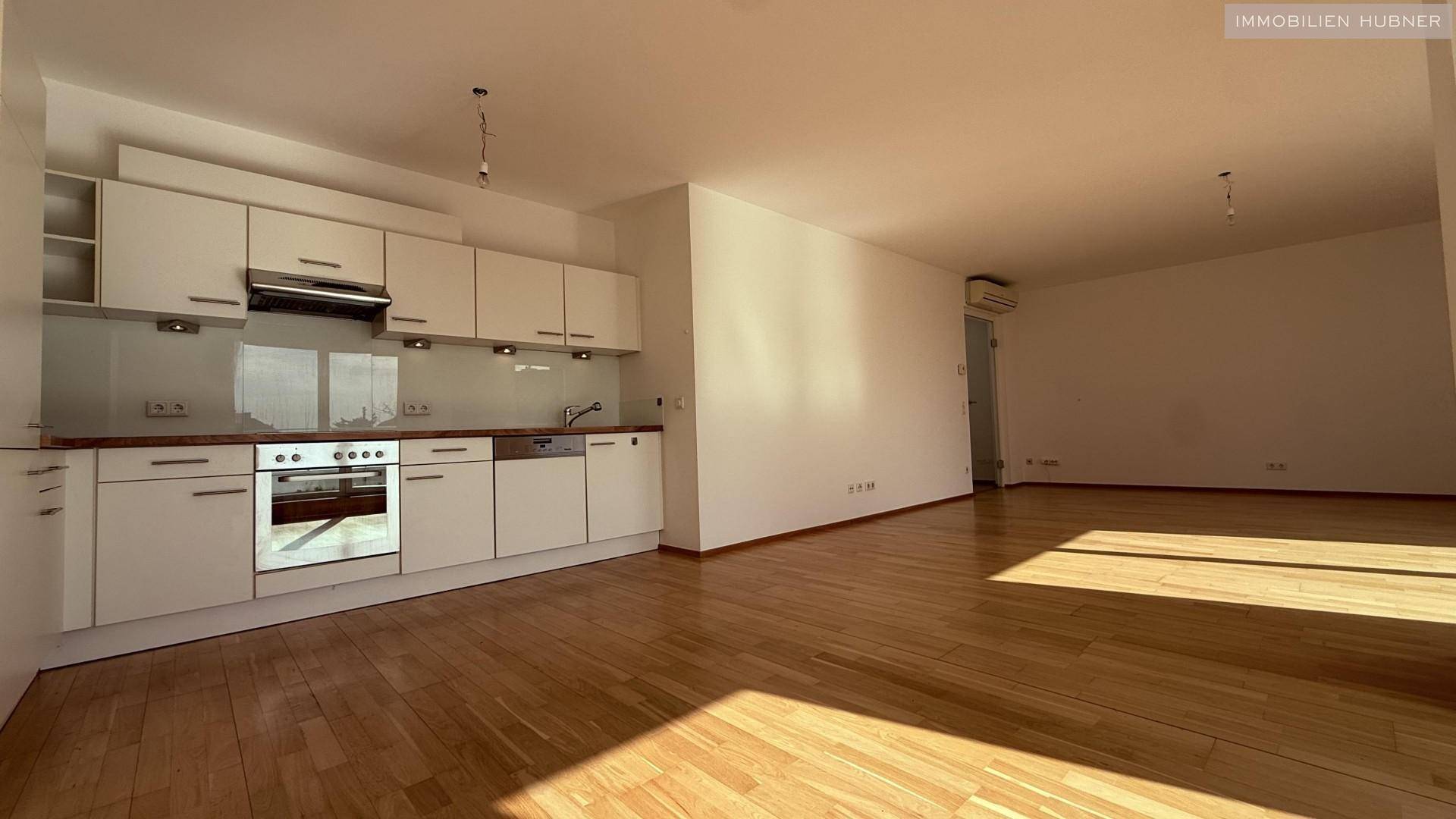 Moderne Einbauküche mit weißen Schränken und Holz-Arbeitsplatte, offen zum Wohnbereich.