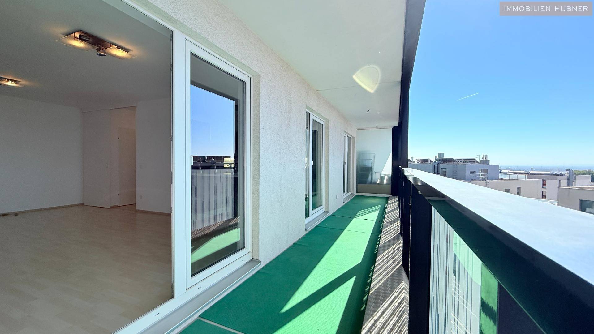 Langer Balkon mit grünem Kunstrasen und Blick auf die Stadt, zugänglich vom Wohnbereich.
