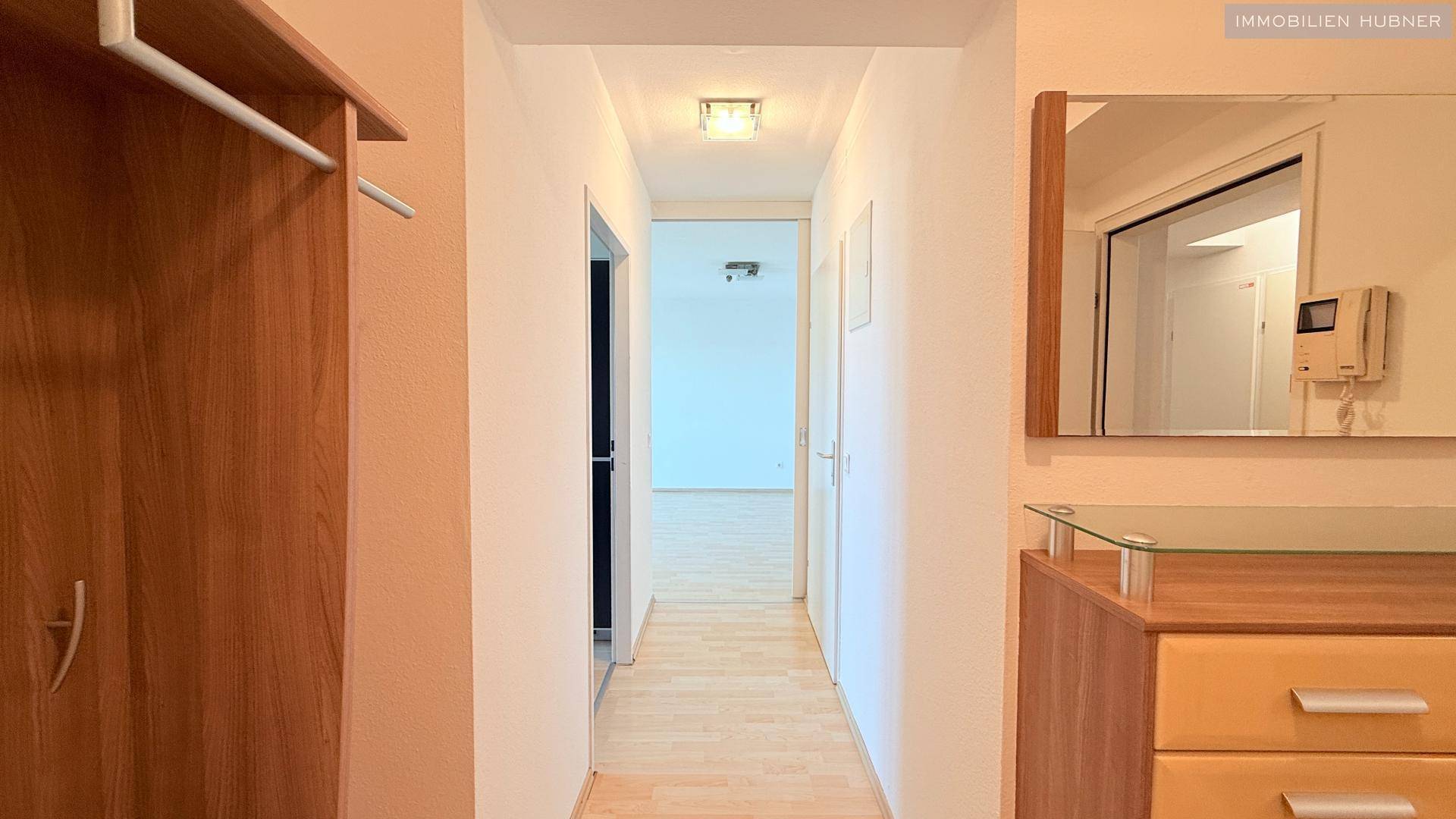 Heller Flur mit Parkettboden, Garderobe und Spiegel, der zu weiteren Räumen führt.
