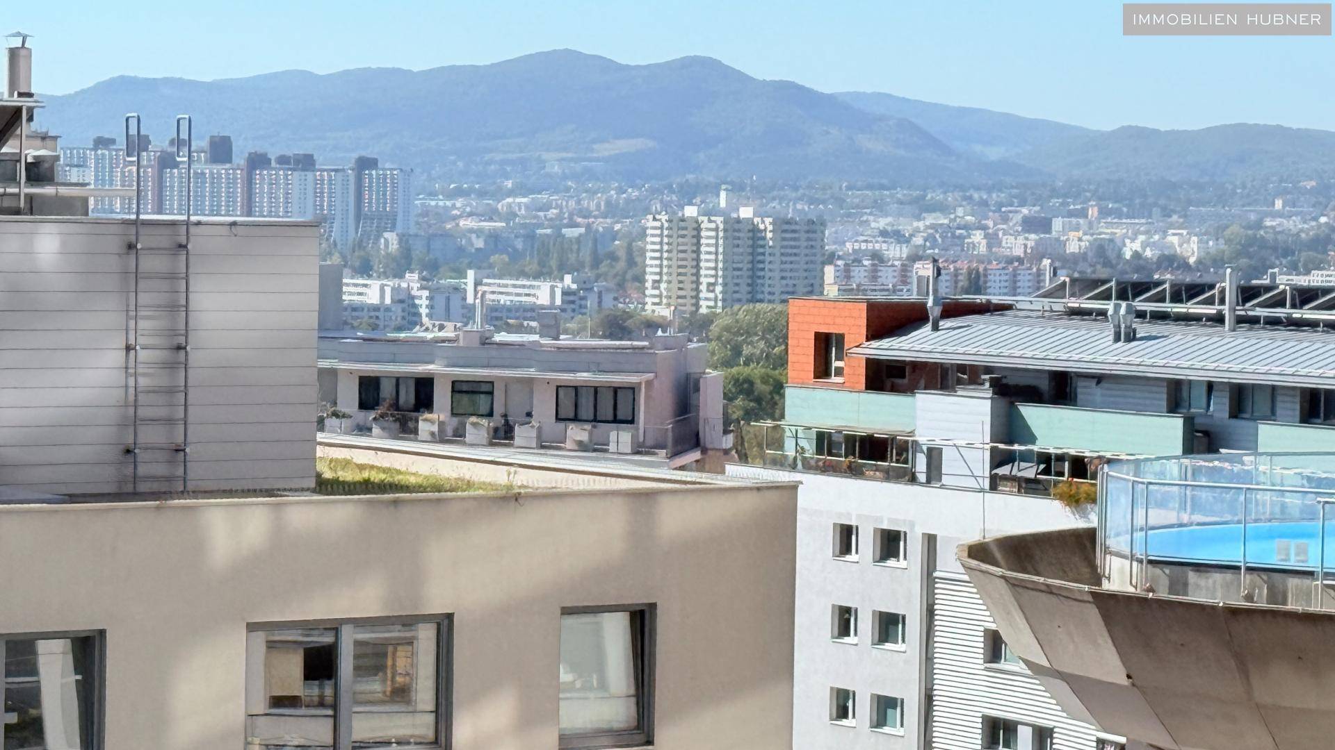 Panoramablick über die Stadt mit modernen Gebäuden und einer Bergkette im Hintergrund.