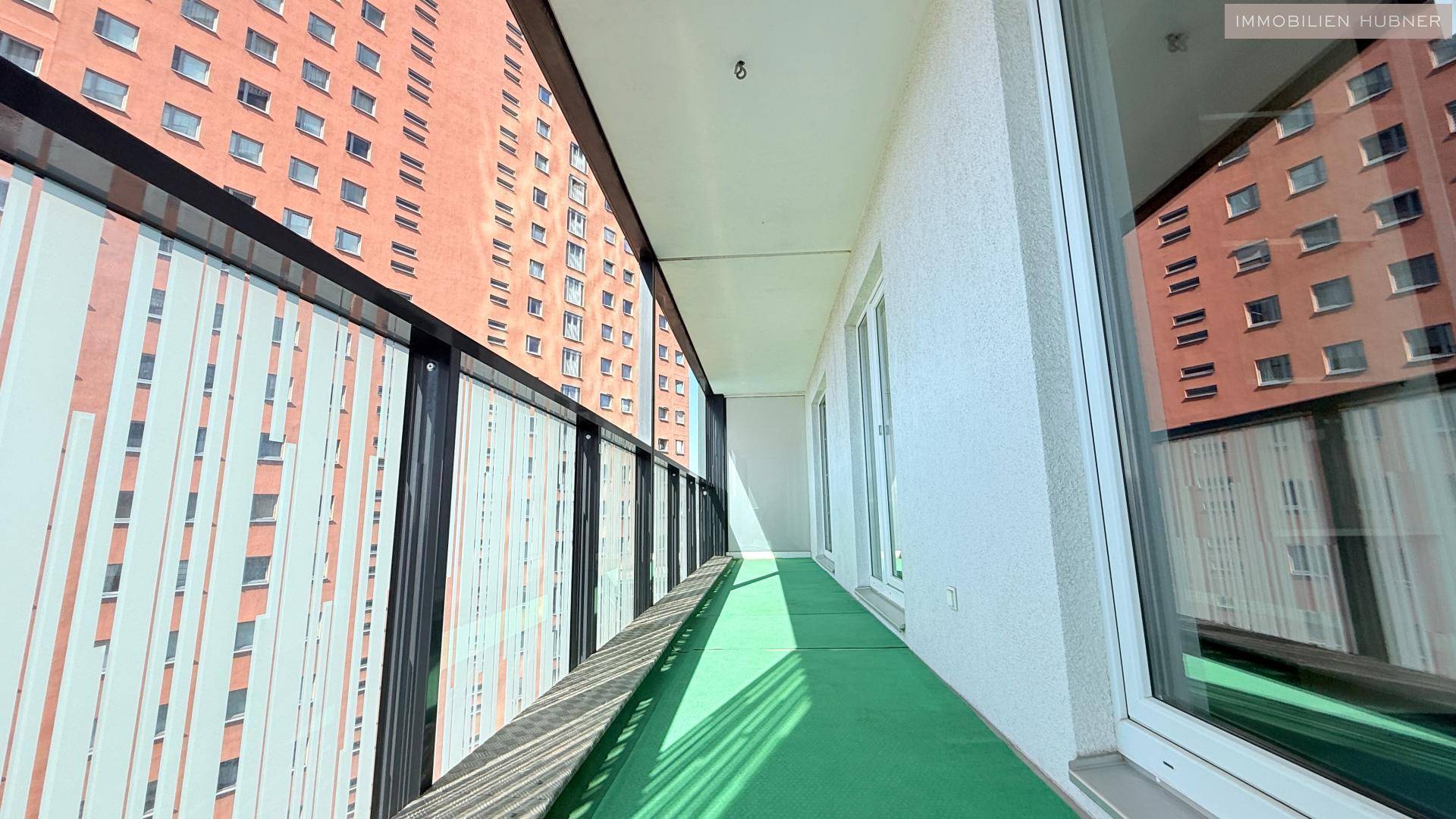 Schmaler Balkon mit grünem Bodenbelag und Blick auf die umliegenden modernen Gebäude.