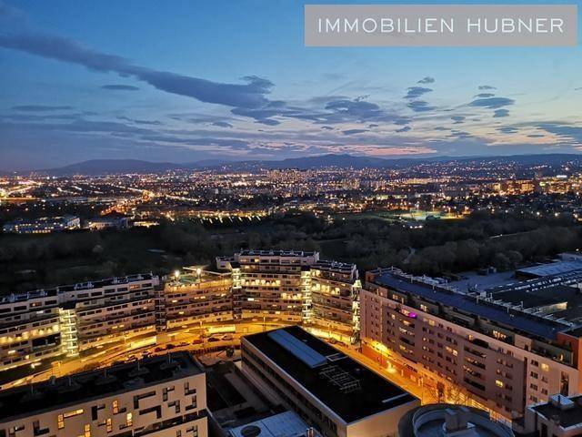 Beeindruckender nächtlicher Panoramablick über die beleuchtete Stadt mit Bergen im Hintergrund.