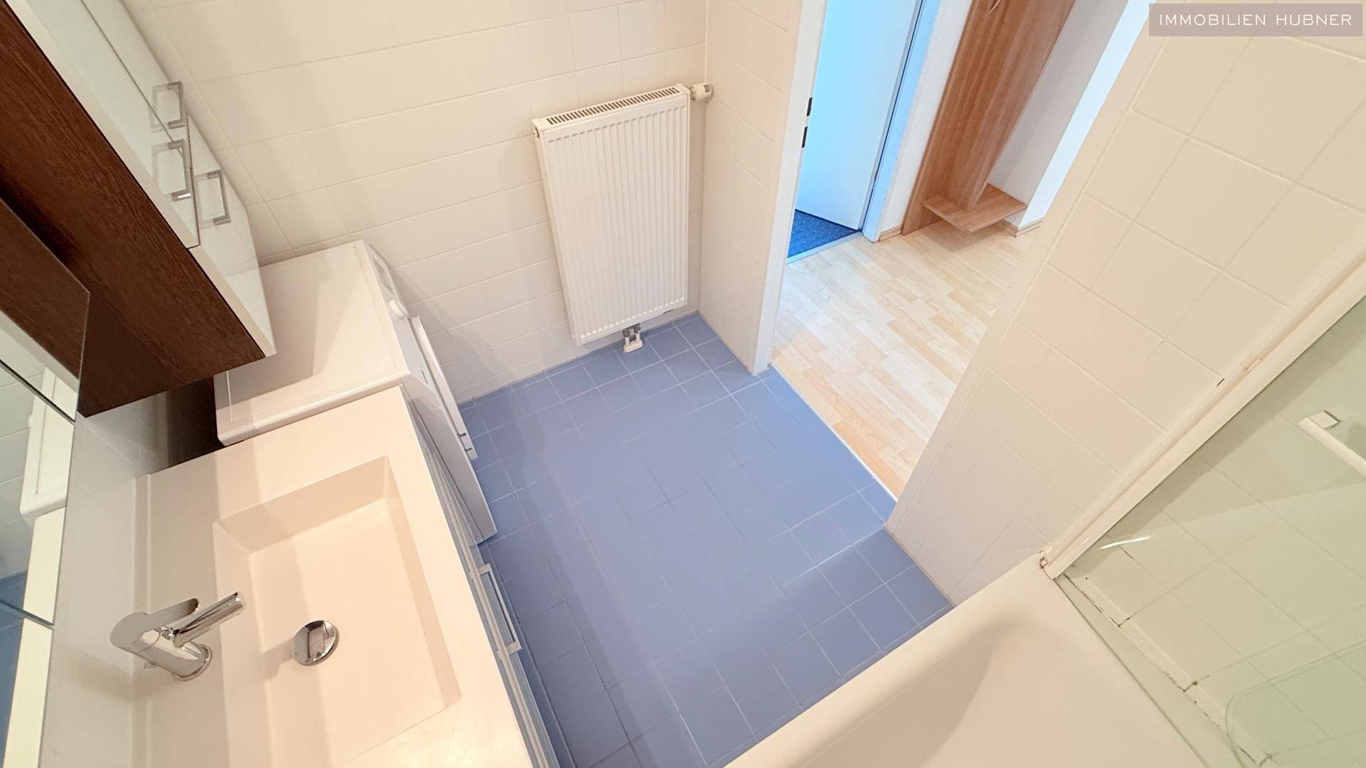 Badezimmer mit hellblauen Fliesen, weißem Waschtisch und Heizkörper, in gutem Zustand.