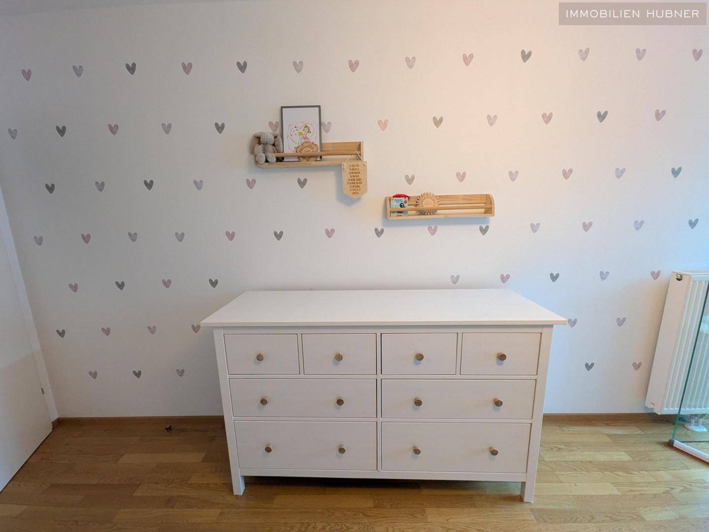Kinderzimmer mit weißer Kommode und herzförmigen Wandstickern, die eine spielerische Atmosphäre schaffen.