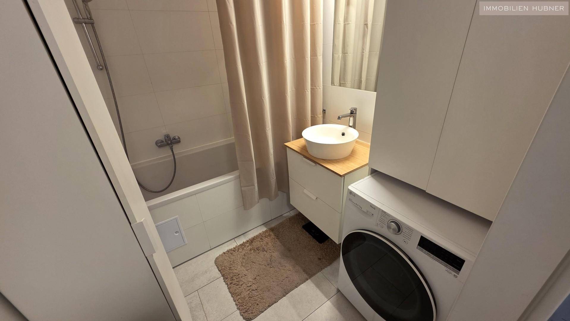 Modernes Badezimmer mit Badewanne, Waschbecken und integrierter Waschmaschine für Komfort.