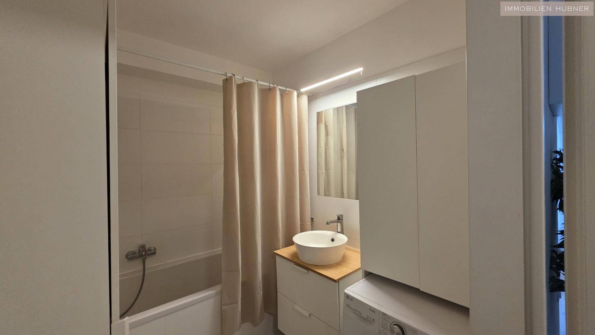 Funktionales Badezimmer mit Badewanne, Duschvorhang und schlichtem Waschtisch mit Spiegelschrank.