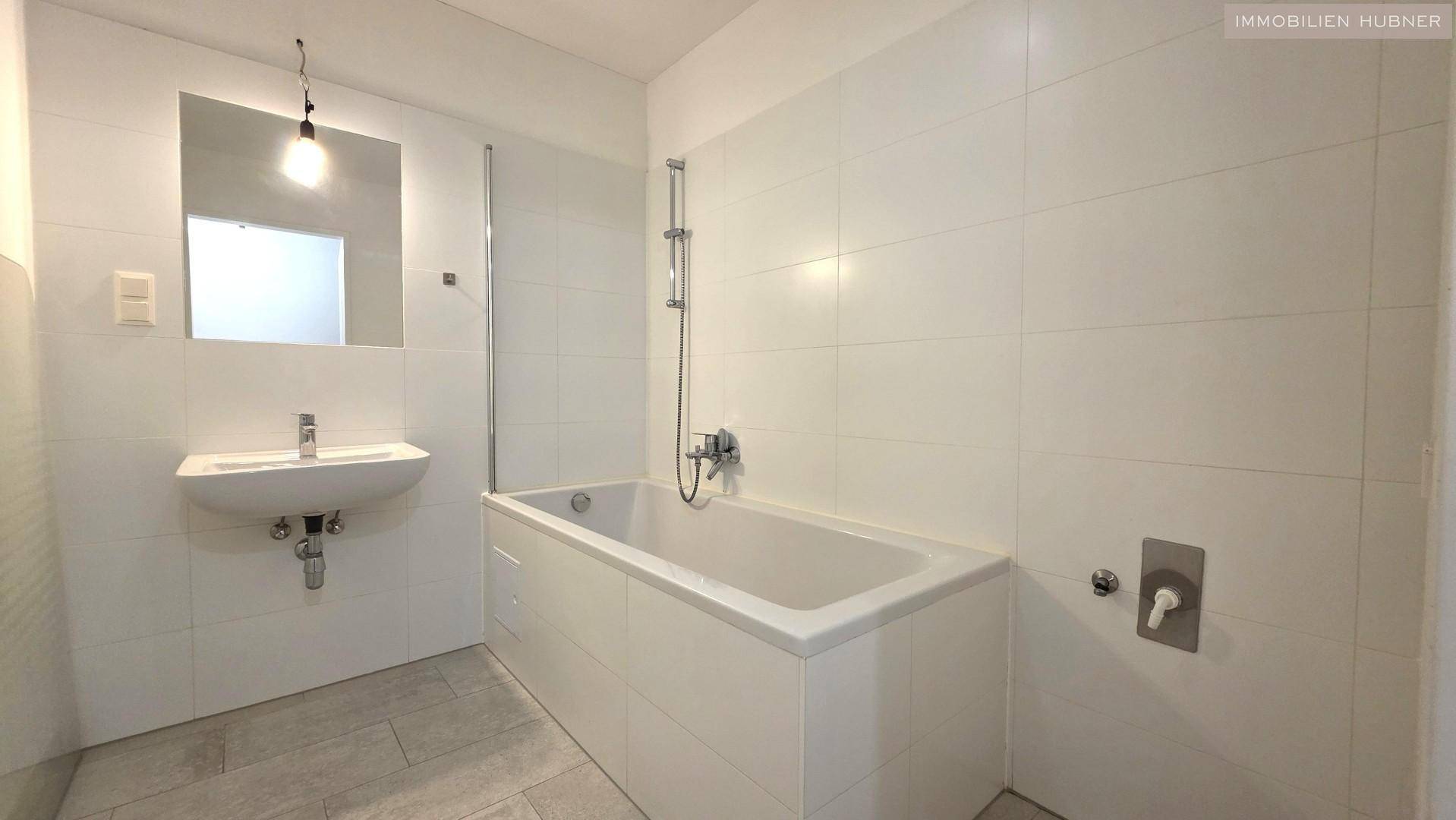 Modernes Badezimmer mit Badewanne, Dusche, Waschbecken und weißen Wandfliesen.