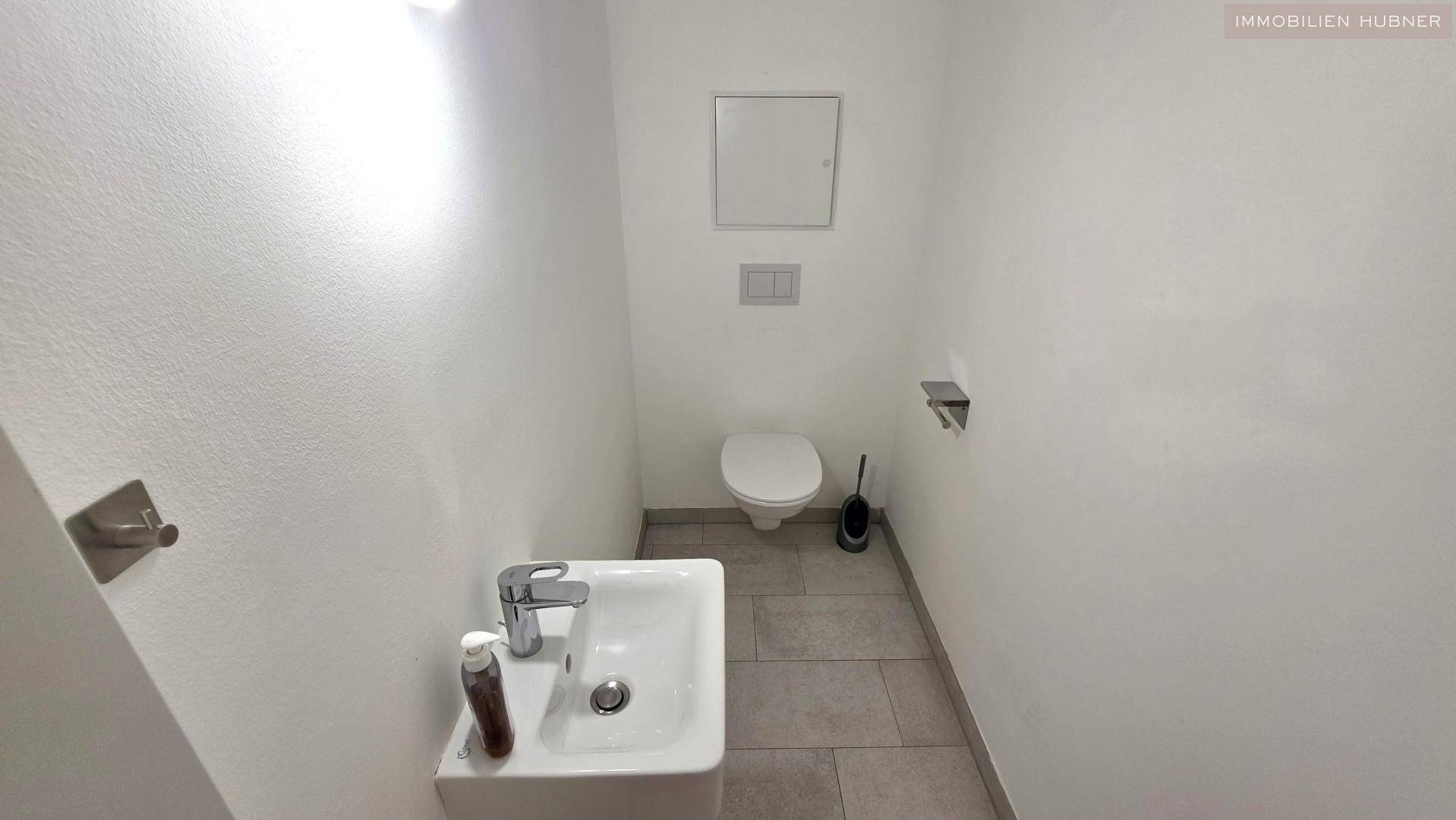 Modernes Gäste-WC mit Wand-WC, kleinem Waschbecken und grauen Bodenfliesen.