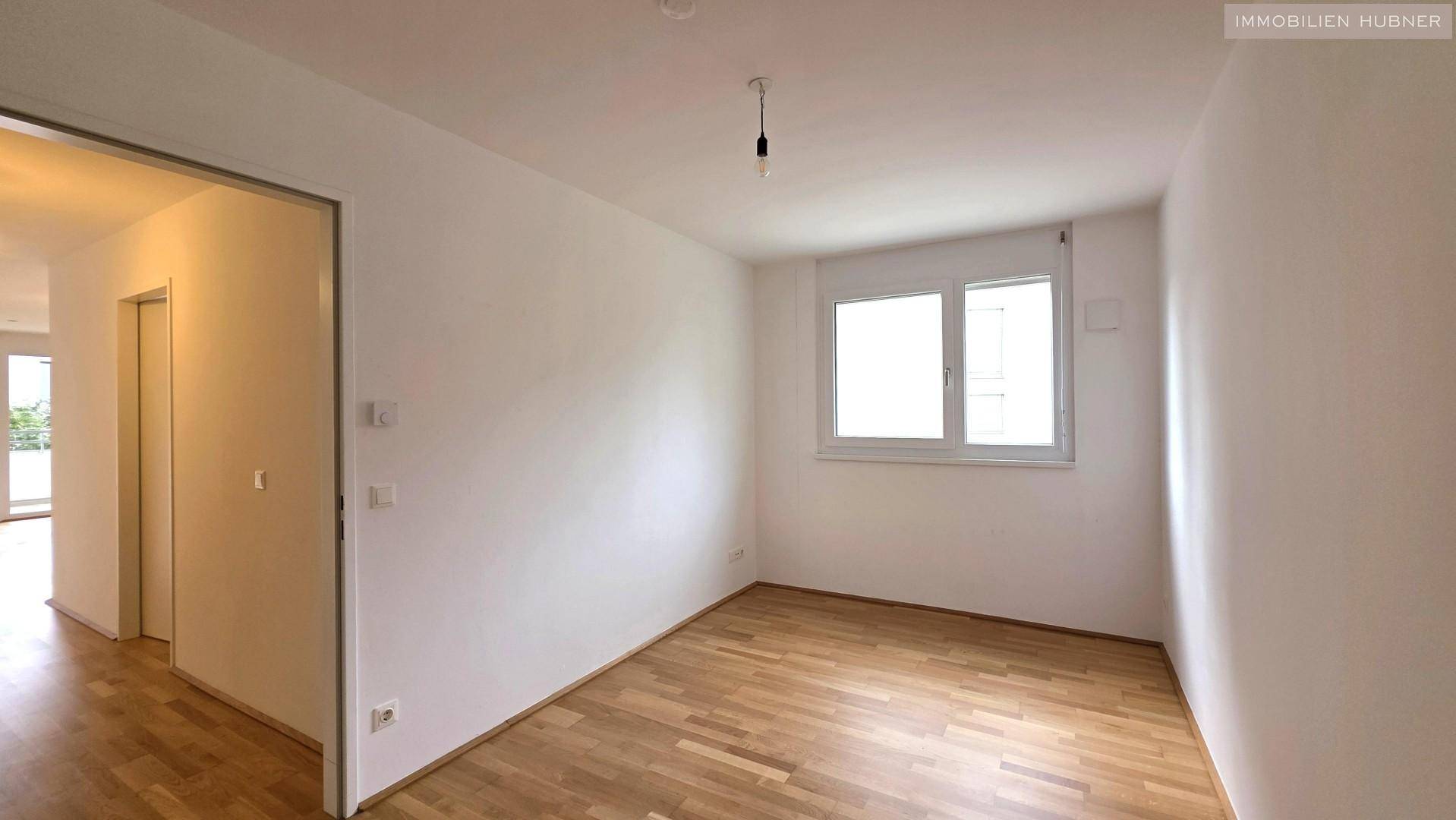 Helles Schlafzimmer mit Parkettboden und großem Fenster, unmöbliert und bezugsfertig.