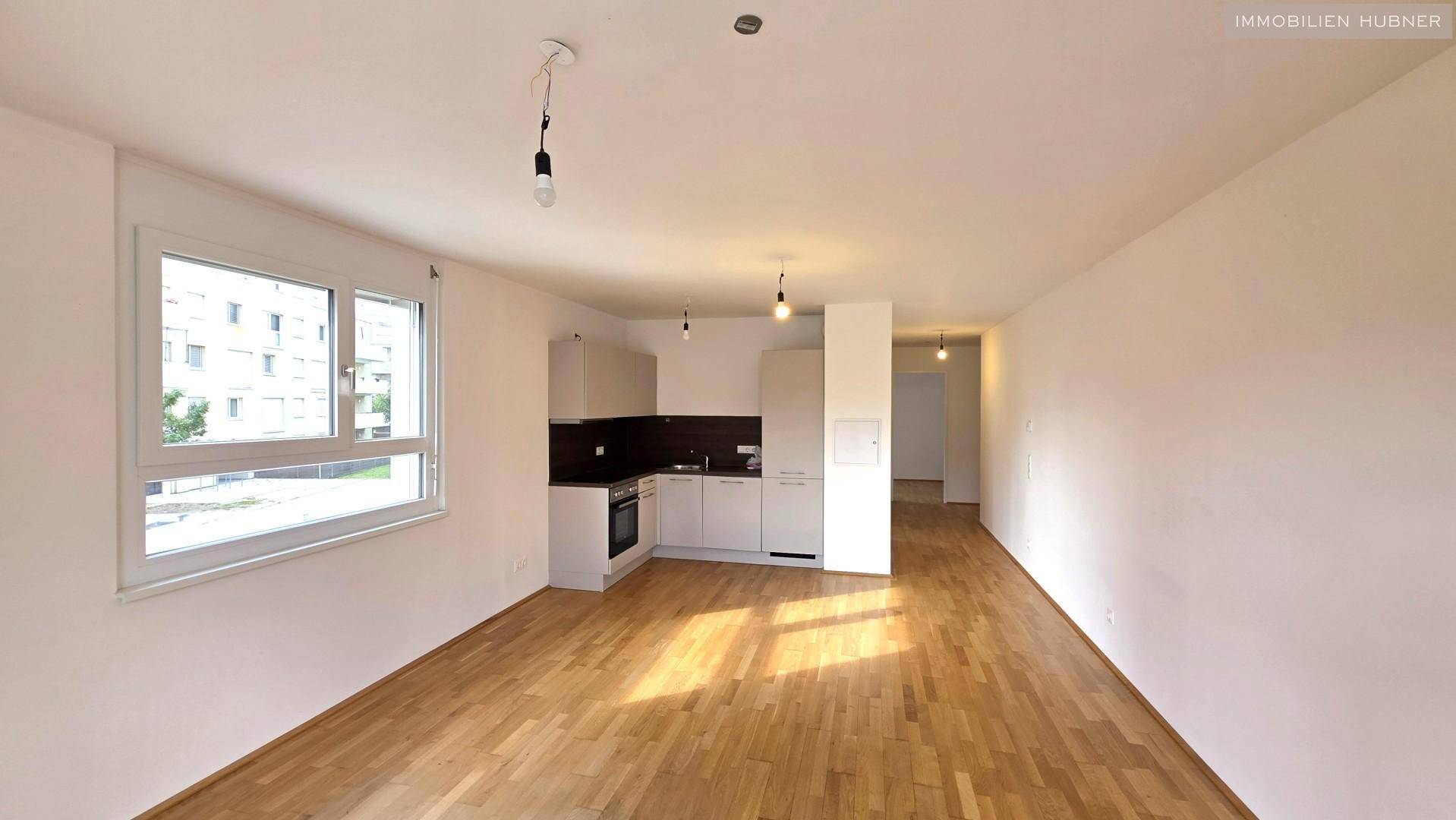 Geräumiger Wohnbereich mit offener Küchenzeile, Parkettboden und großen Fenstern.