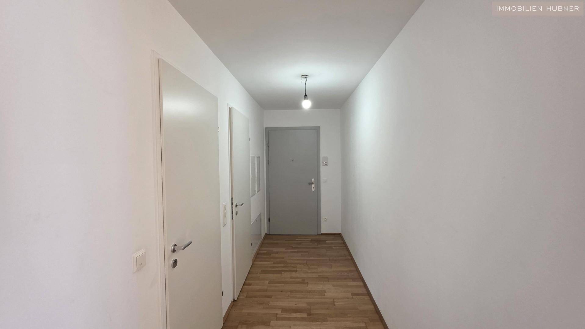 Heller Flur mit Parkettboden und weiß gestrichenen Wänden, führt zur Eingangstür.