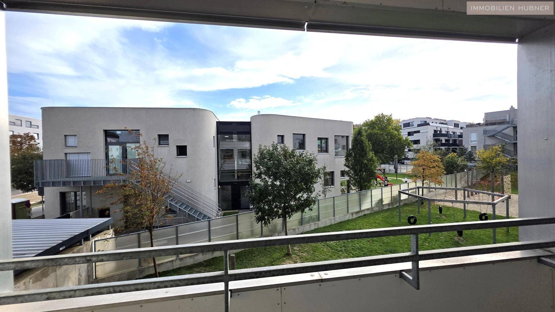 Blick vom Balkon auf die moderne Wohnanlage mit Grünflächen und Spielplatz.