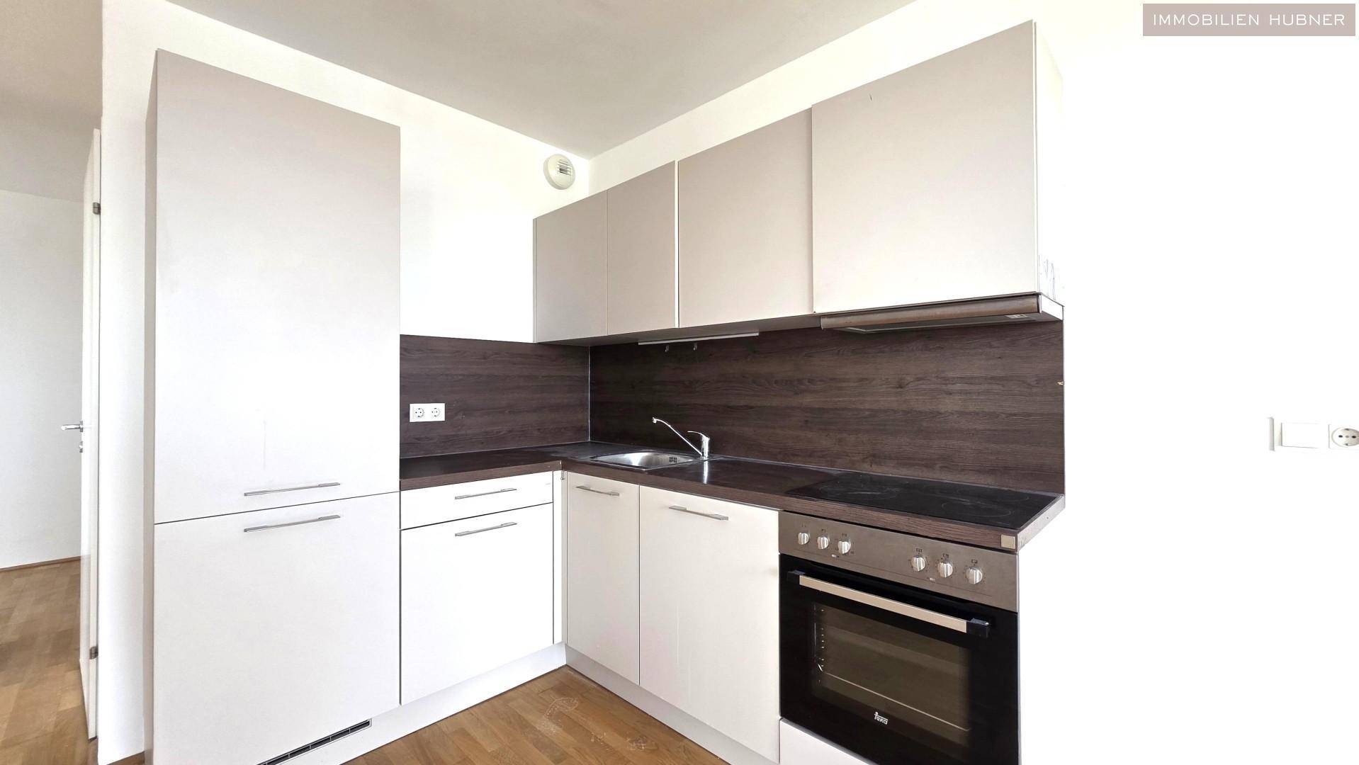 Moderne Einbauküche mit hellen Schränken, dunkler Arbeitsplatte und integriertem Backofen.
