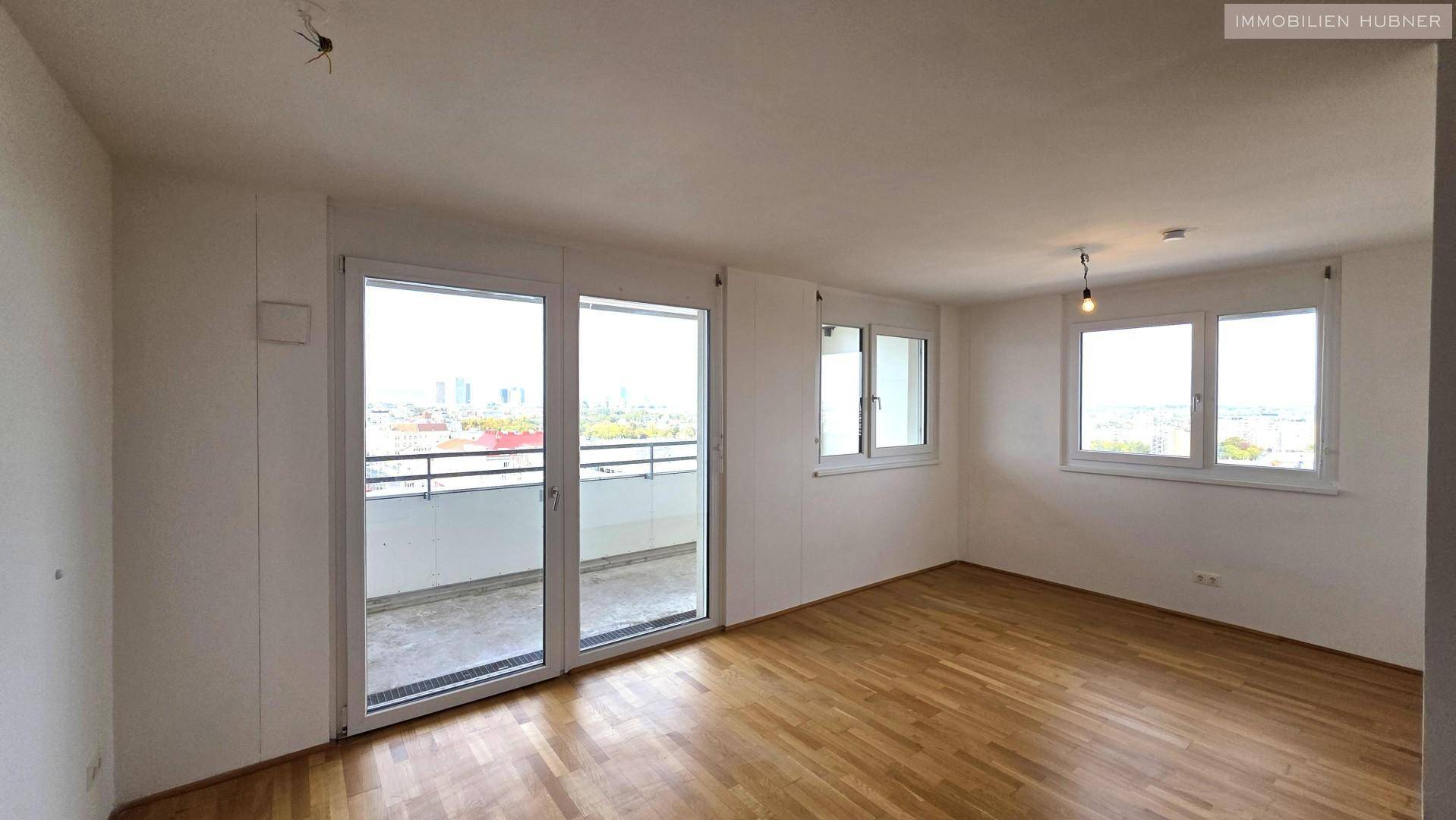 Geräumiges Wohnzimmer mit Parkettboden, großen Fenstern und Zugang zu einem Balkon.