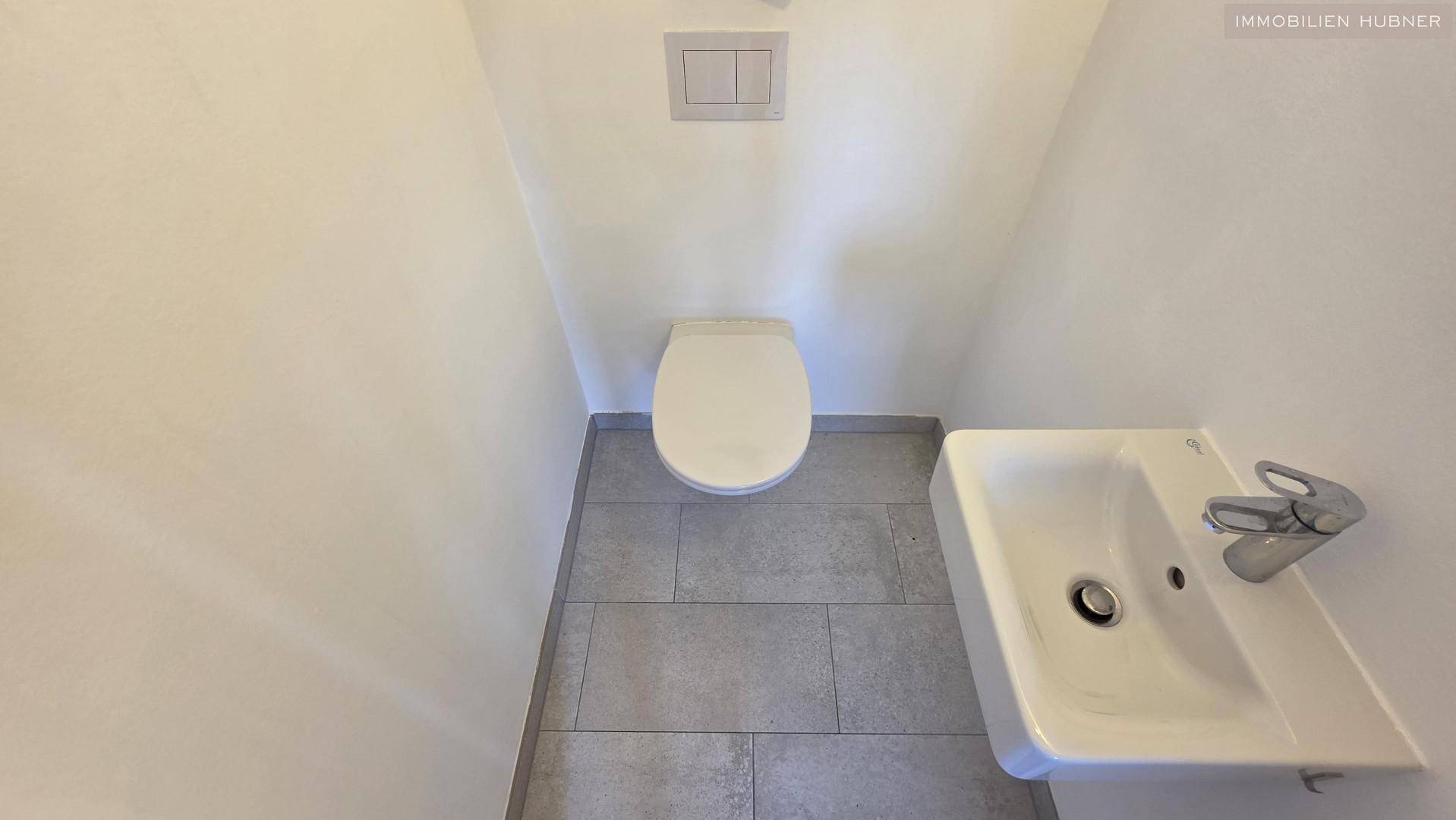 Kleines Gäste-WC mit Wand-WC, Waschbecken und grauen Bodenfliesen.